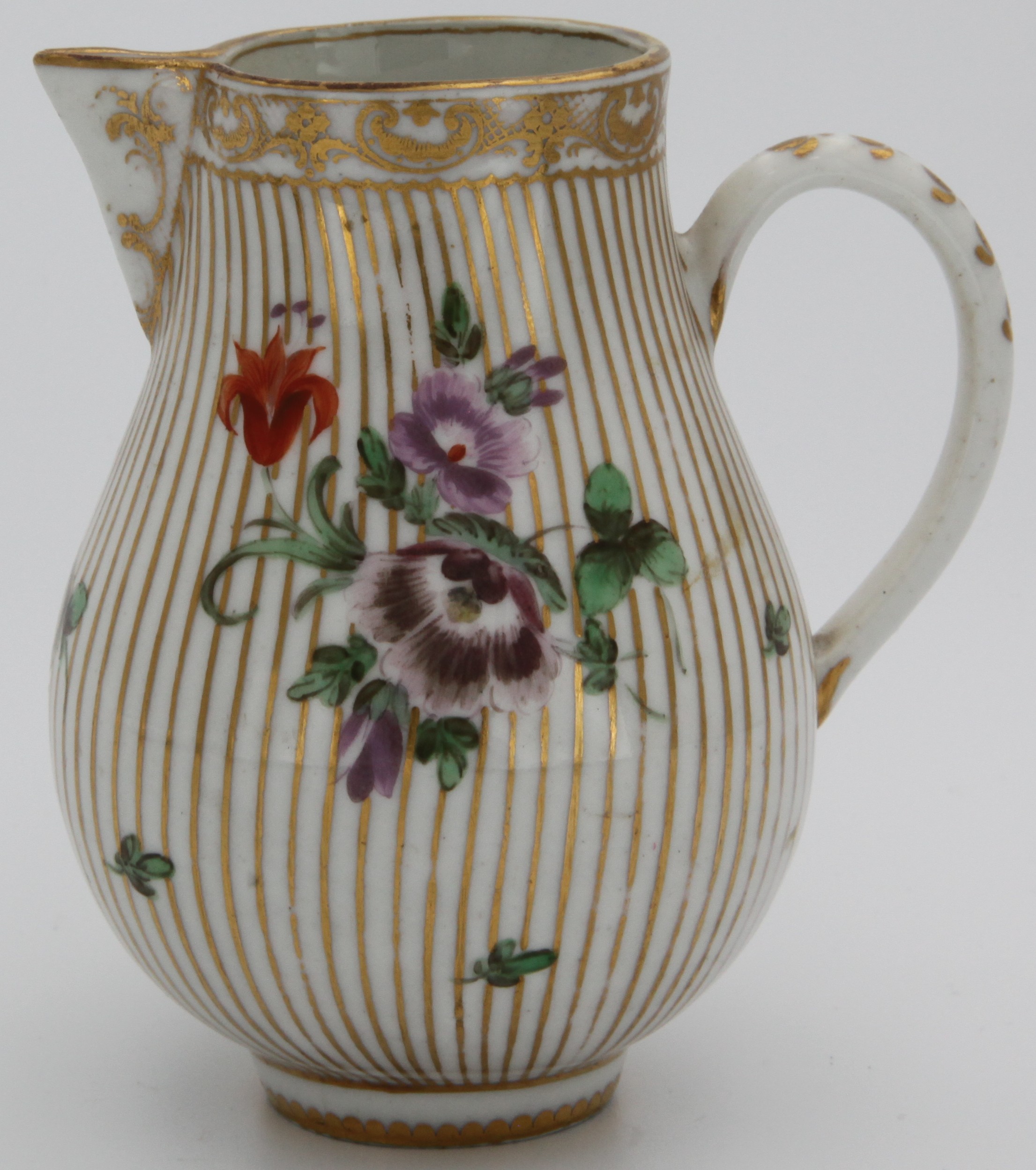 A Bristol baluster-shaped sparrow beak milk jug, with loop handle, painted in coloured enamels with a spray of flowers and leaves, and scattered flowers, on a gilt striped ground, the rim with a gilt flower head and 'C' scroll band, circa 1775, blue painted X mark.