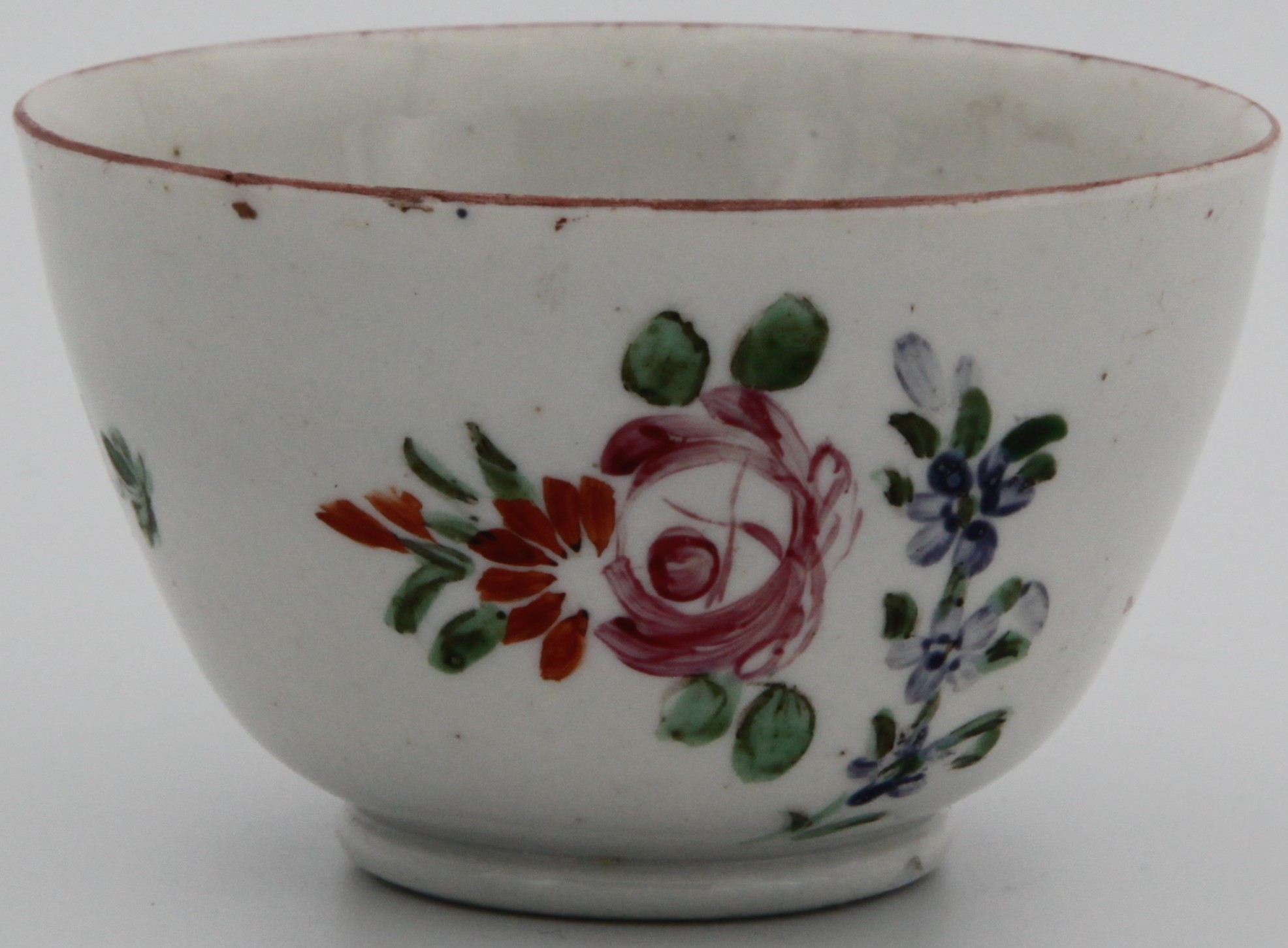 A Bristol tea bowl, painted (rather poorly) with a  bouquet of colourful summer flowers, iron red line border, marked with blue X and 21.