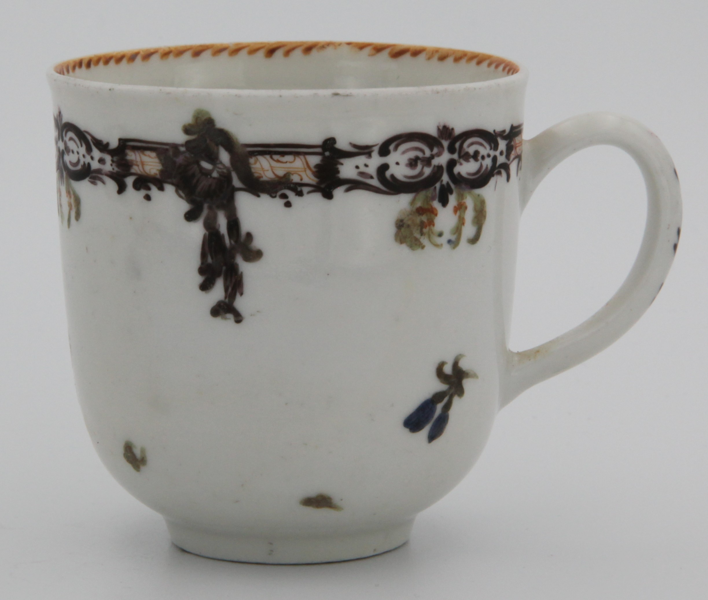 A Bristol coffee cup, with unmoulded handle decorated in purple, painted with a stylised purple band above scattered flowers, the interior with angular orange dentil rim, c. 1770. No mark.