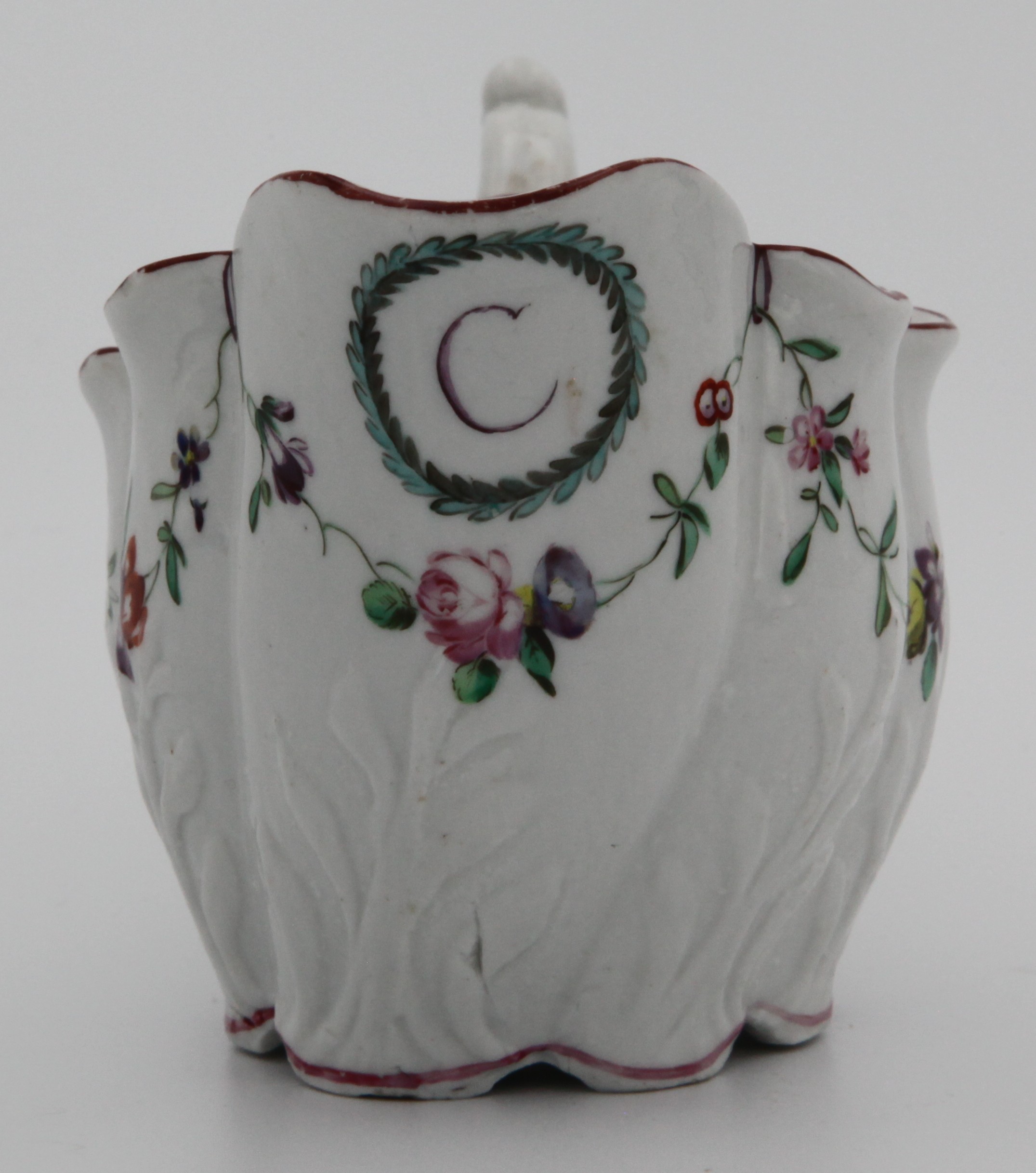 A rare Bristol low Chelsea ewer, in relief with wrythen foliage, painted with floral swags suspended from purple loops hanging from an iron red line border, shaped handle, initial 'C' in puce surrounded by a blue and green leaf wreath under spout, marked with an X, c. 1770