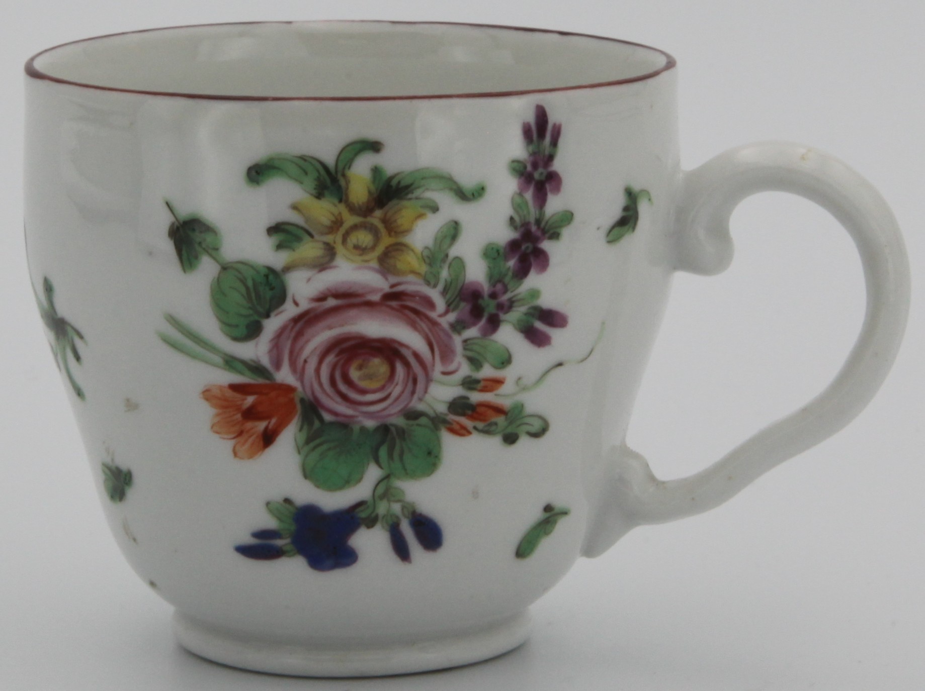 Bristol coffee cup of ogee form and with ear-shaped handle,  painted with spray of flowers with central rose and scattered flowers and leaves with iron red rim c. 1775-78. Mark: underglaze blue crossed swords with dot and painted blue X.