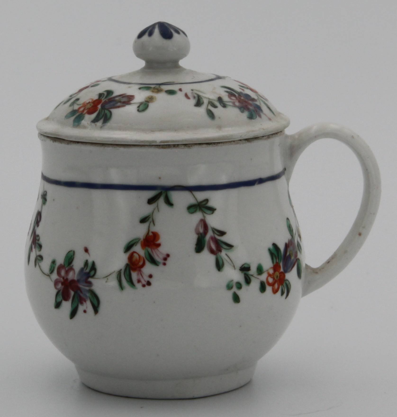 A rare Bristol custard cup and cover, with plain handle, painted with festoons of flowers suspended from plain blue line, slightly domed cover, ball finial painted blue,  c. 1770. No mark