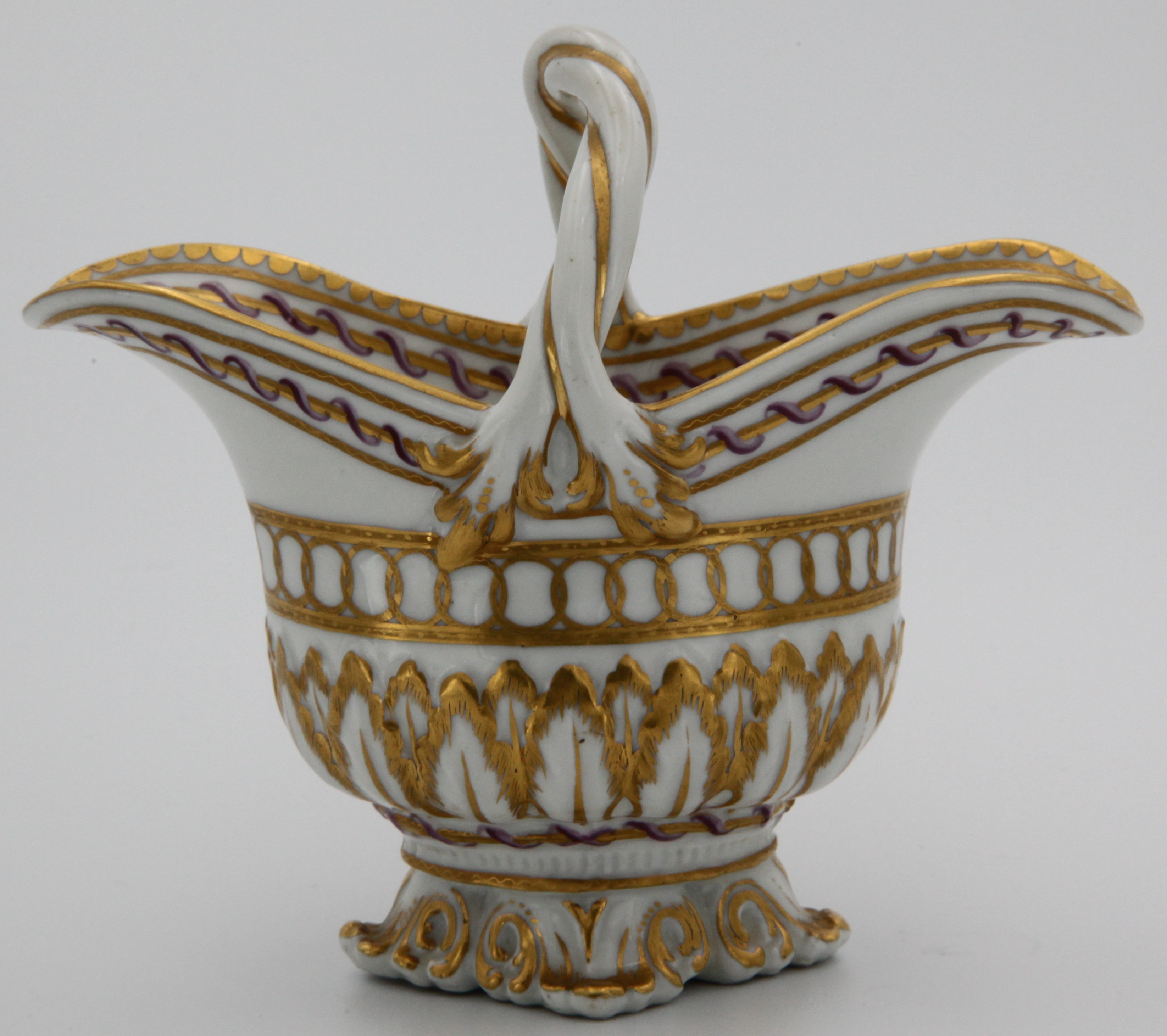 A fine Bristol double-lipped cream jug, with entwined double-stranded handle with stiff-leaf surface moulding to the lower bowl and a moulded Rococo foot, heavily decorated in giltwith an upper band of overlapping gilt circles between two gilt lines below a gilt line encircled by a pink and purple ribbon again betwen two gilt lines and repeated on the inside and topped off with gilt dentil rim. circa 1775. Mark:blue X gilt 1.
