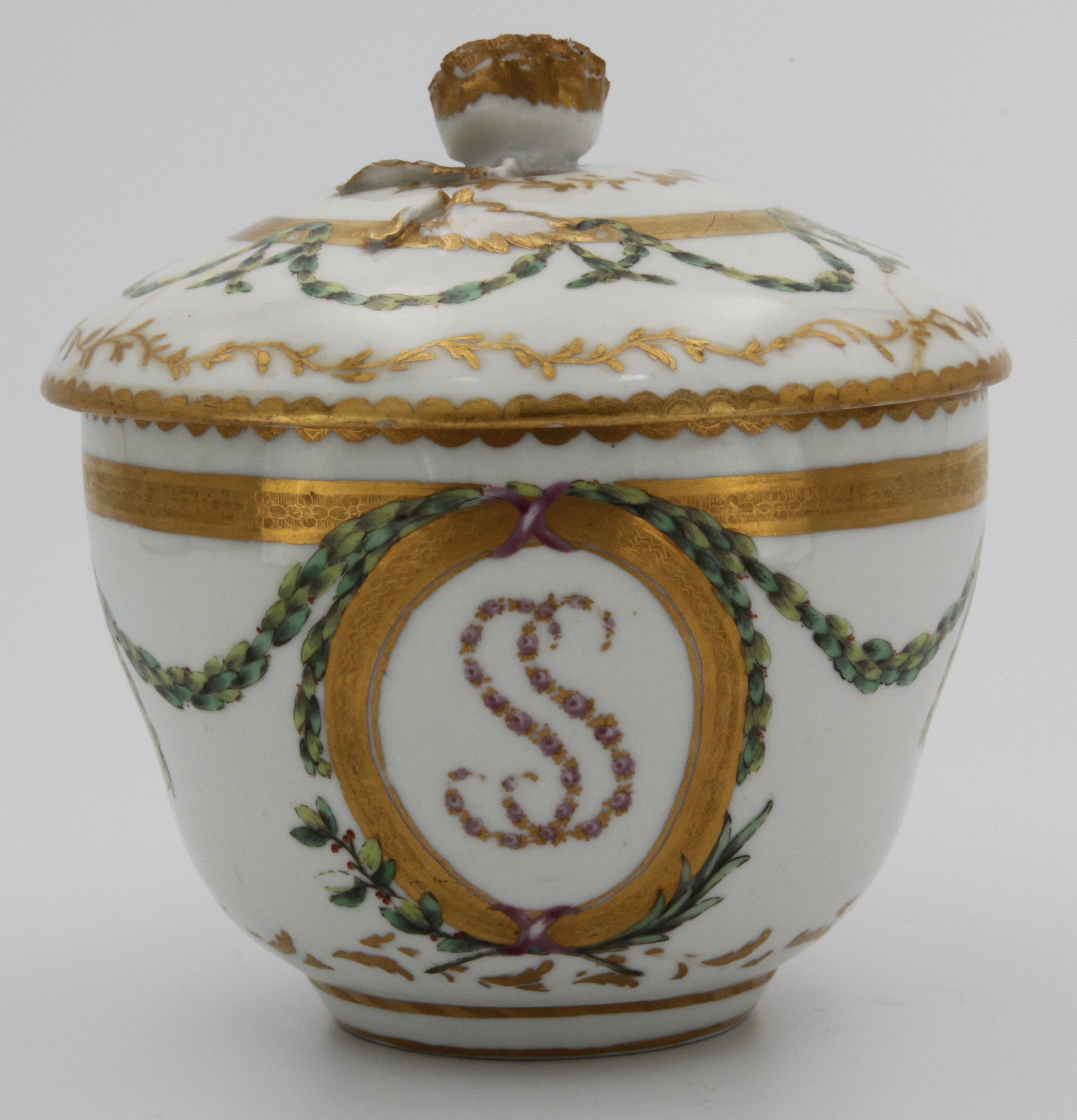 A Bristol sucrier and cover from the Smith service, of ogee shape, the cover with finely modelled and gilt-decorated flower knop, painted in enamels with green laurel garlands resting on oval gilt panels, two containing the arms of Smith in black, red and gilt and two larger panels containing the initials SS (Sarah Smith) in tiny pink and gilt garlands and all three panelse resting on gilt fronds, all between heavy gilt lines and under gilt dentil rim, circa 1774-75. Unusual marks: blue X together with puce tin. A.1., the 1 matching Henry Bone's typical numeral