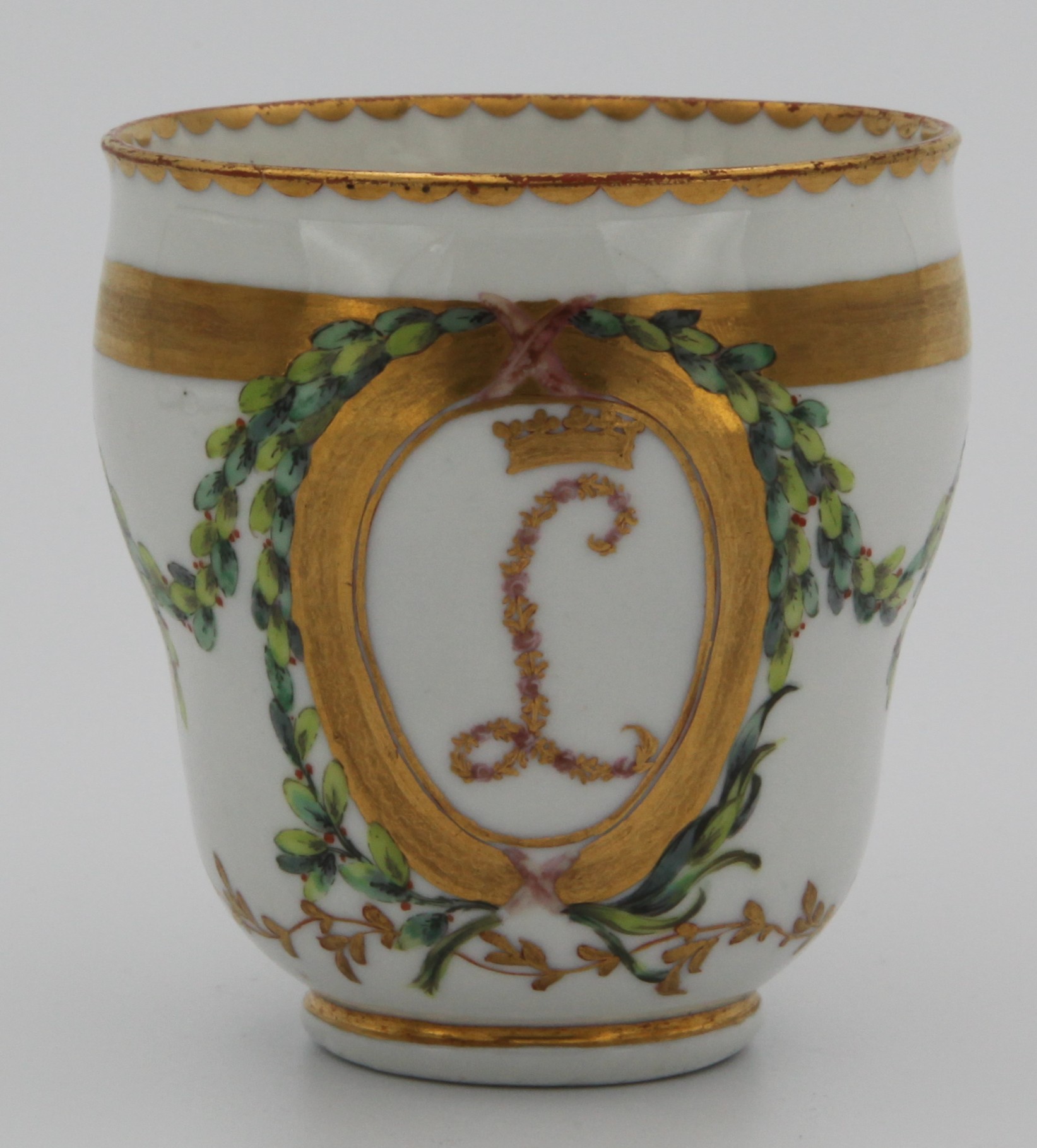 A rare Bristol ogee-shaped coffee cup from the Leinster service, with moulded loop handle, decorated in coloured flower heads with the intial L beneath a gilt ducal coronet, within oval gilt panels, the cup with two grisaille head and shoulder studies of young men, united by green and iron red laurel swags, gilt line, leaf scroll and dentil borders, circa 1775, blue painted X and numeral 3 in gilt.