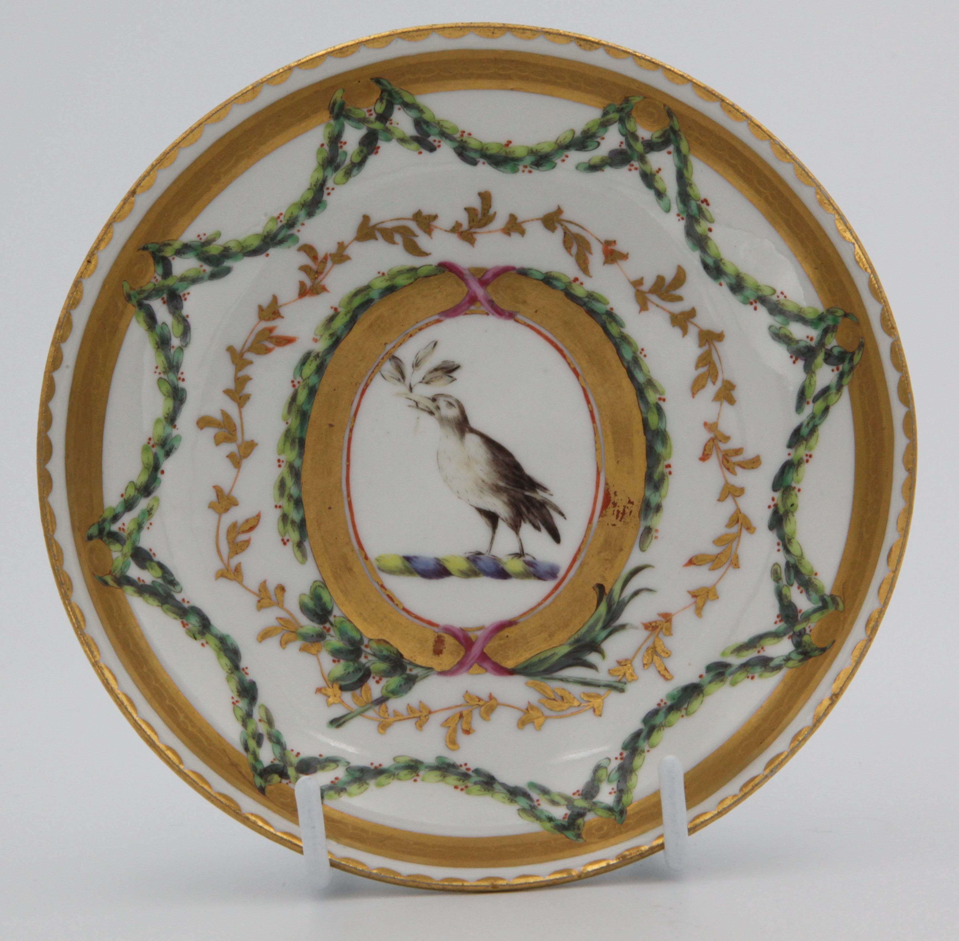 A Bristol ogee shaped coffee saucer, from the Chough Service, painted with a bird crest, with leaves in its beak, probably for Tothill of Peamore, Devon, within oval cartouches, and with sepia profile medallions, united by laurel swags, within gilt tooled, leaf and dentil bands, circa 1774-75, blue painted X marks. See F S Mackenna, Plymouth and Bristol Porcelain, page 68, plate 27, for a plate from this service.