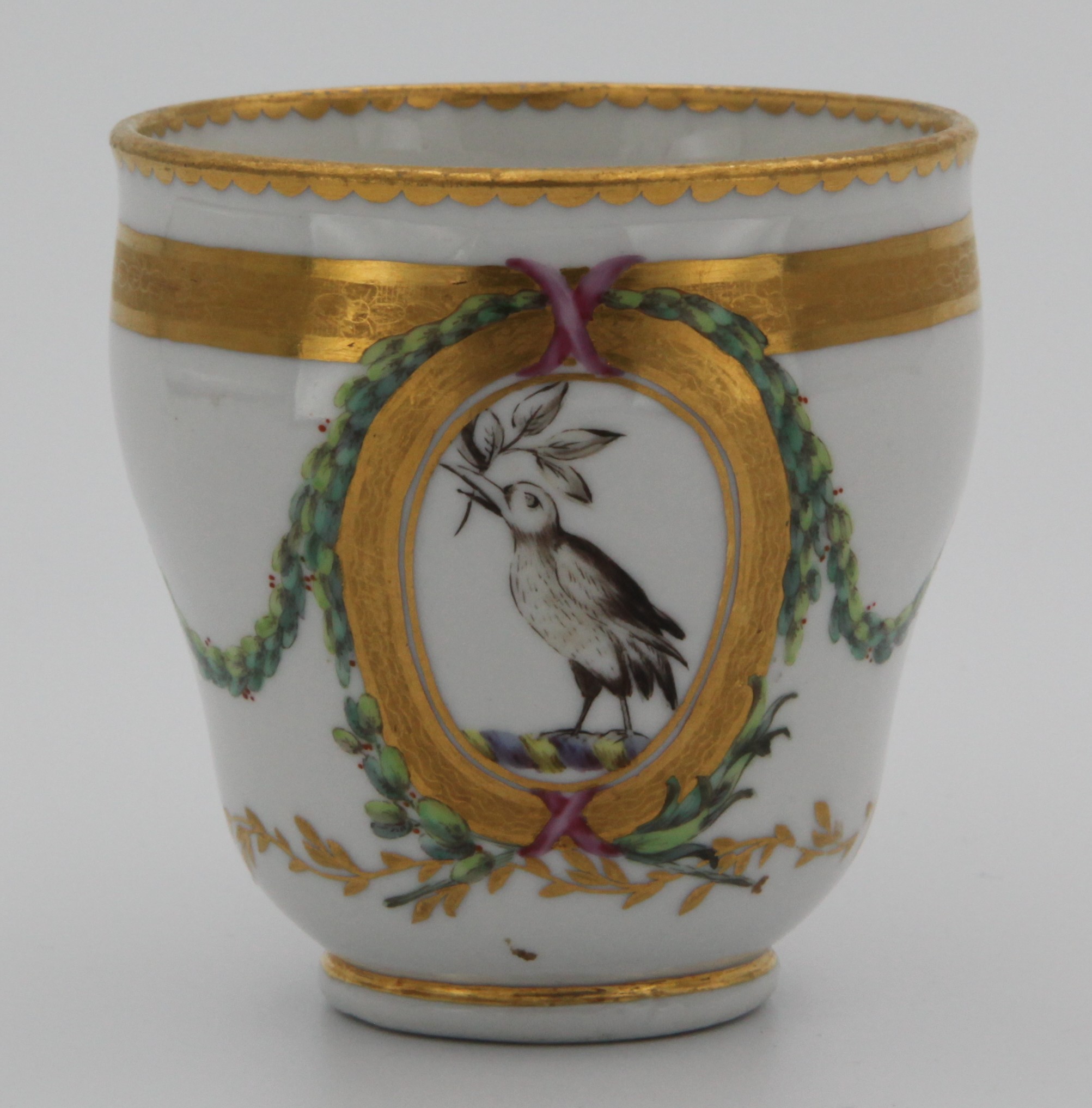 A Bristol ogee shaped coffee cup, from the Chough Service, with harebell-moulded and gilt-decorated handle, painted with a bird crest, with leaves in its beak, probably for Tothill of Peamore, Devon, within oval cartouches, and with sepia profile medallions, united by laurel swags, within gilt tooled, leaf and dentil bands, circa 1774-75, blue painted X marks. See F S Mackenna, Plymouth and Bristol Porcelain, page 68, plate 27, for a plate from this service.