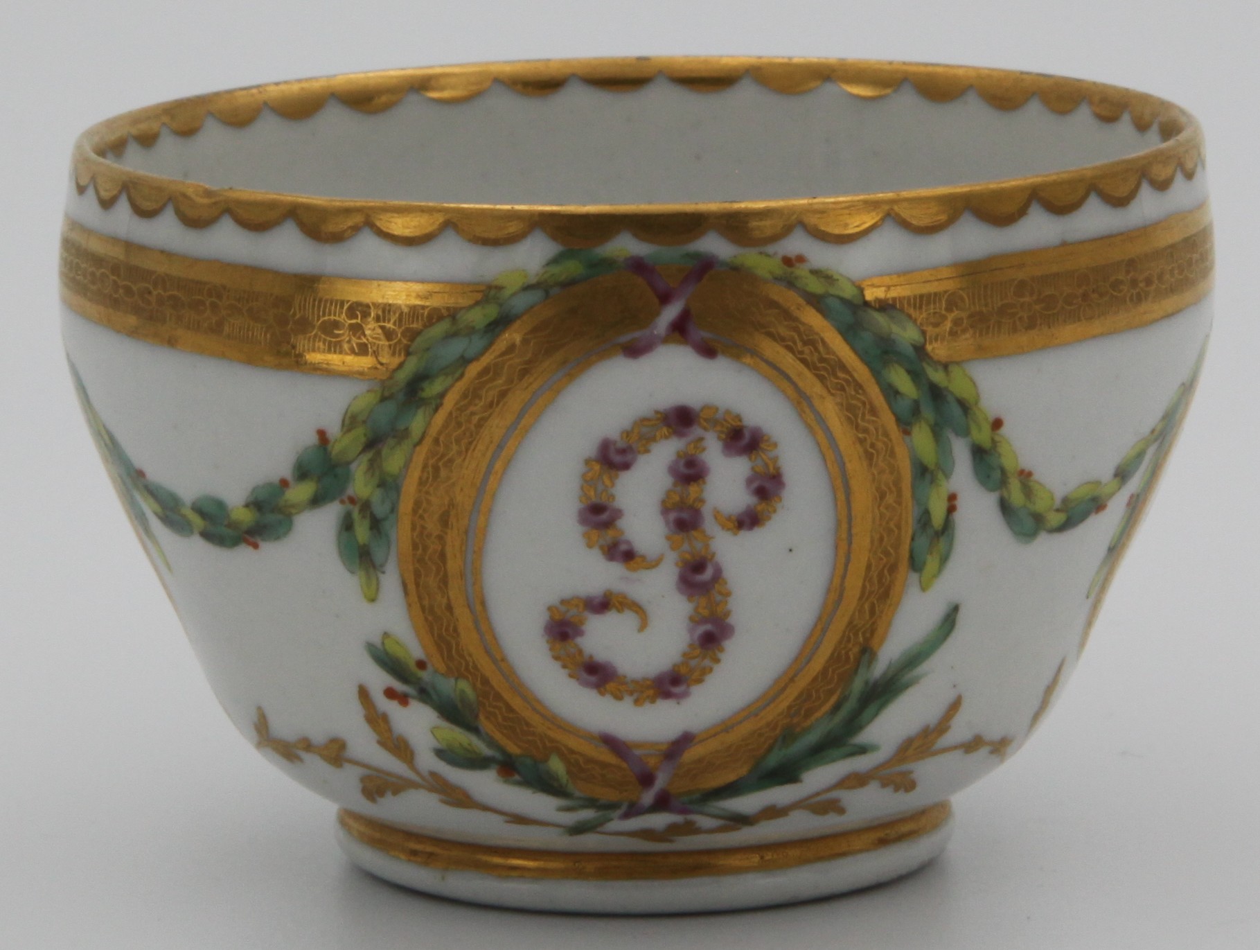 A Bristol tea cup from the Plumer Service, with initial P in pink roses and gilt, within a tooled oval gilt panel, and with grisaille portrait medallions, within green, iron red and gilt laurel and leaf scroll borders, gilt dentil rims, circa 1774-75, blue painted X marks. See F S Mackenna, Plymouth and Bristol Porcelain, number 29, for the sucrier and cover from this service