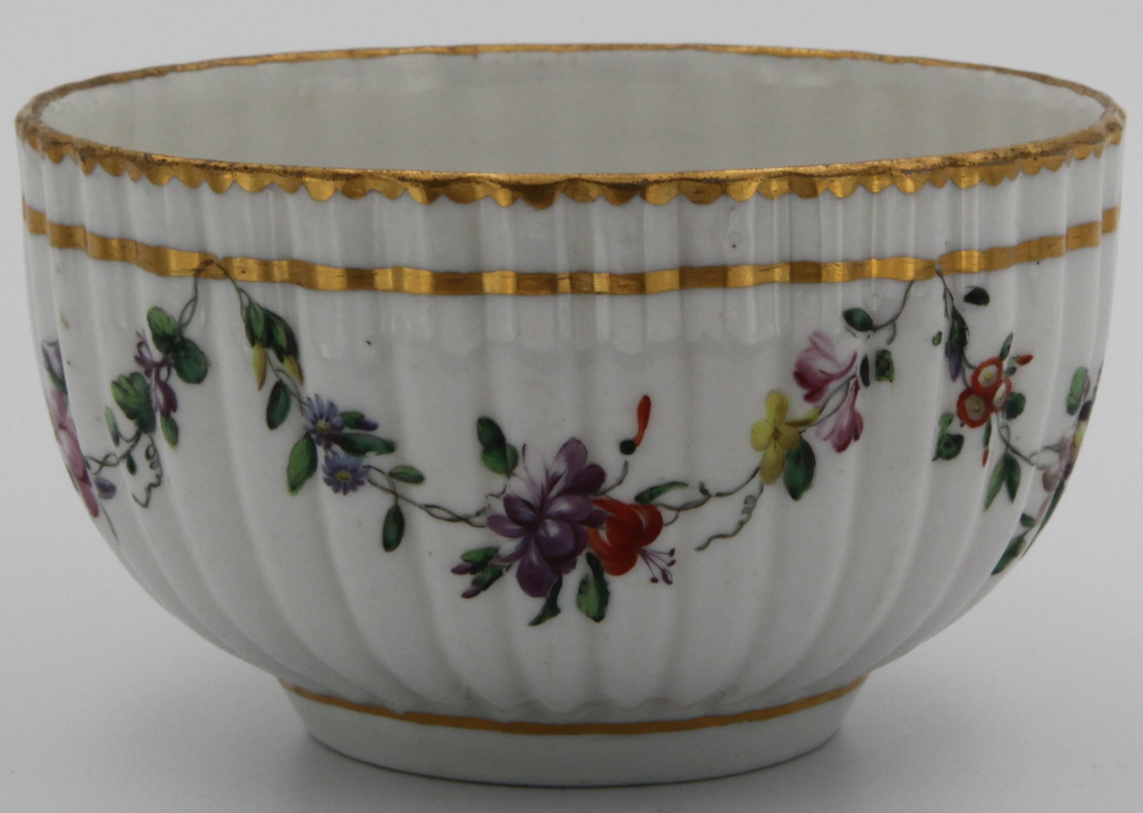 A fine Bristol fluted porcelain bowl finely painted with polychrome foliate swags suspended from a heavy gilt band, gilt dentil rim, floral spray to bottom of the bowl, the underside with underglaze blue cross mark and numeral 2.