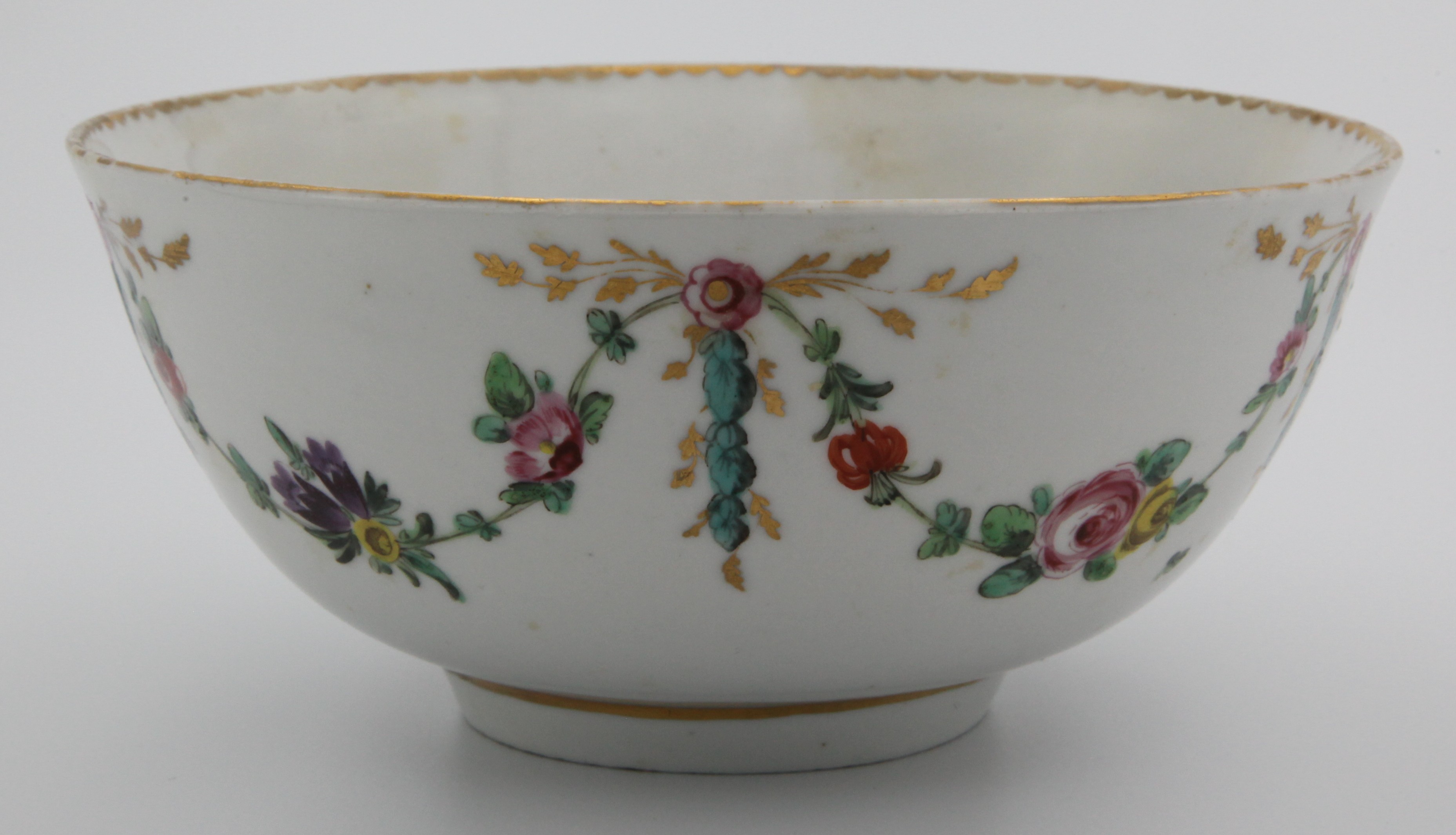 A Bristol round bowl, the exterior painted in coloured enamels with swags of flowers and leaves, suspended from pink rosettes, from which issue gilt leaf scrolls and laurel, the interior painted with a pink rose, gilt dentil rim, circa 1775, numeral 1 in gilt. See Albert Amor Vanessa Stevenson lot 38 for another example