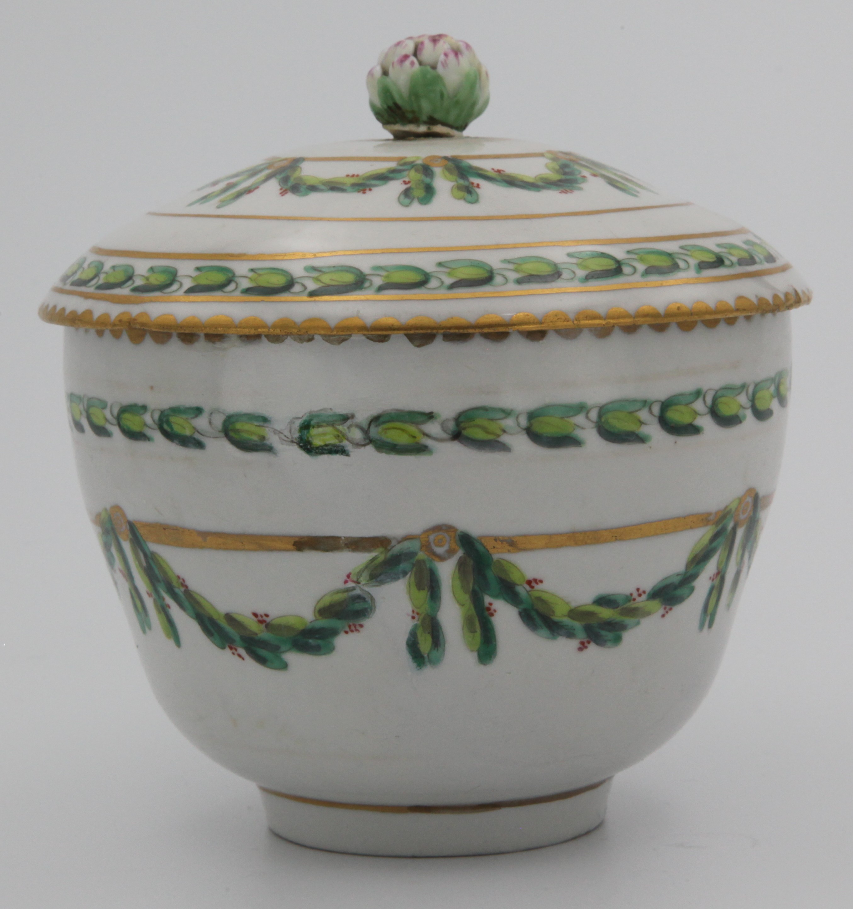 A Bristol ogee-shaped sucrier and cover,  the cover with green and pink painted bud finial, painted in green and iron red with laurel swags, suspended from gilt flower head roundels and bands, within stiff leaf and gilt dentil borders, marked X1. to the base.