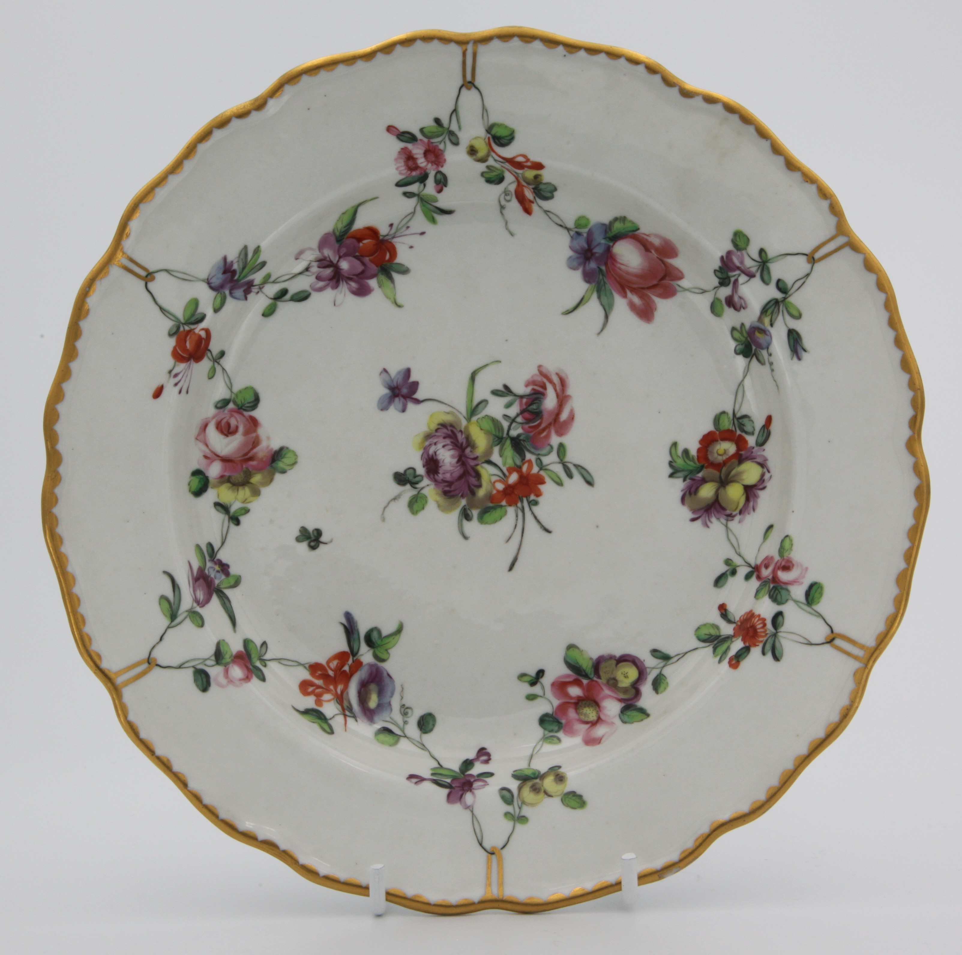 A fine Bristol plate painted with garlands of flowers suspended from gilt rings around a central bouquet, gilt dentil rim, blue Xb mark, circa 1775-80. Double reinforcement ring to base.