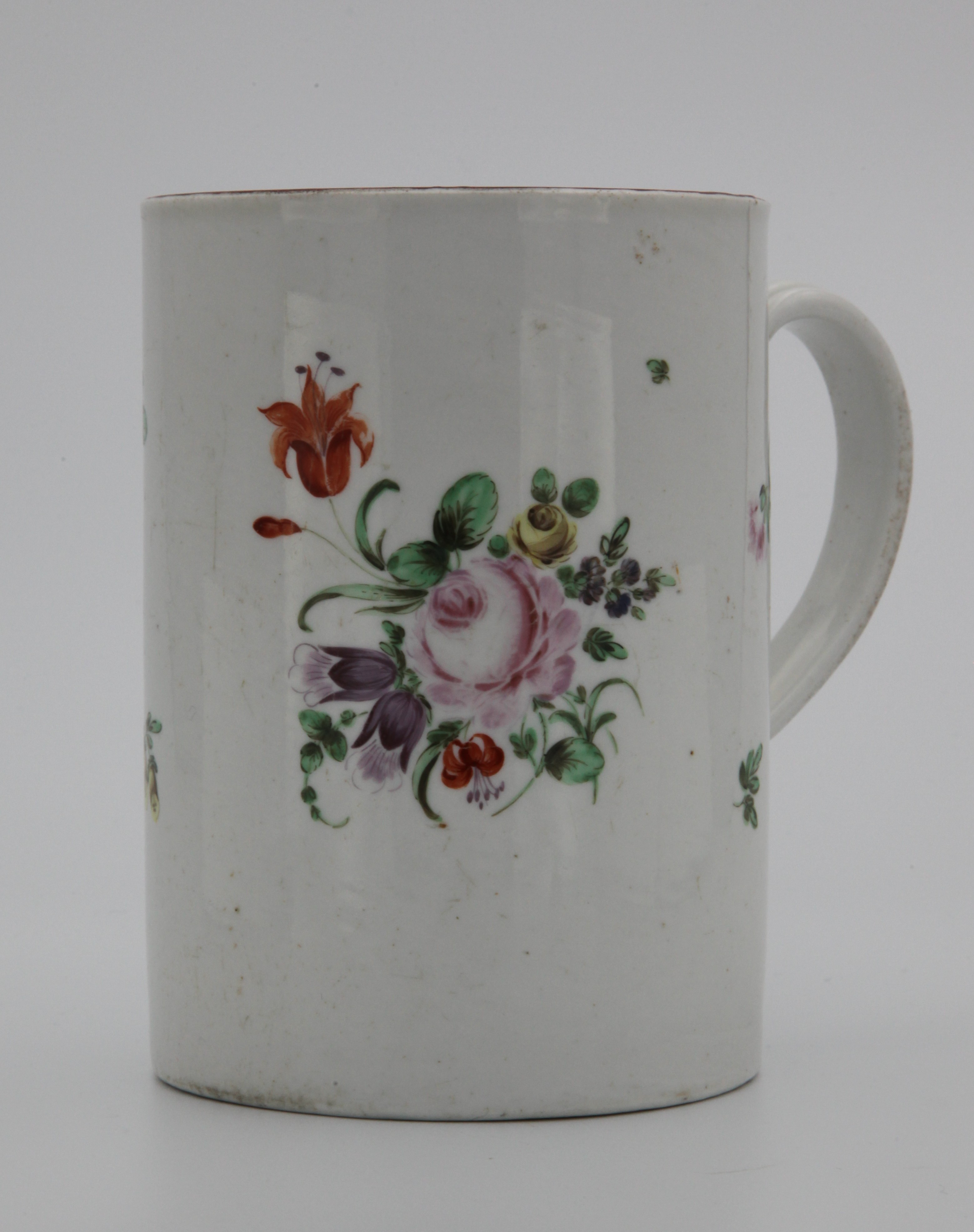 A large Bristol mug with simple undecorated ridged handle, painted in enamels with a spray of flowers to the front and scattered flowers and leaves, iron red rim, circa 1775. Mark X6.