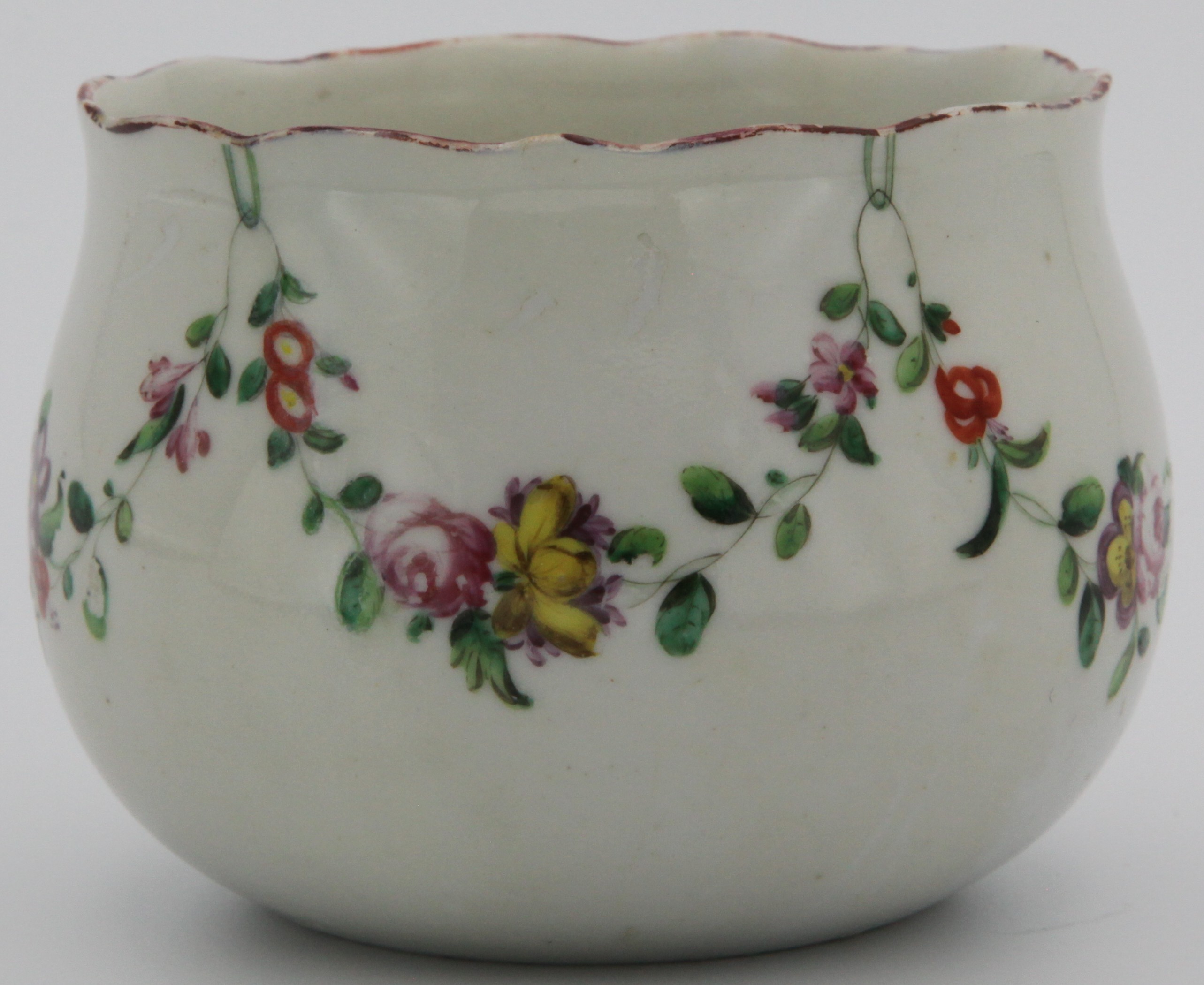 A Bristol finger bowl painted with a garland of flowers and foliage suspended from green rings under iron red rim line, blue X mark, circa 1770-75. Base unfinished