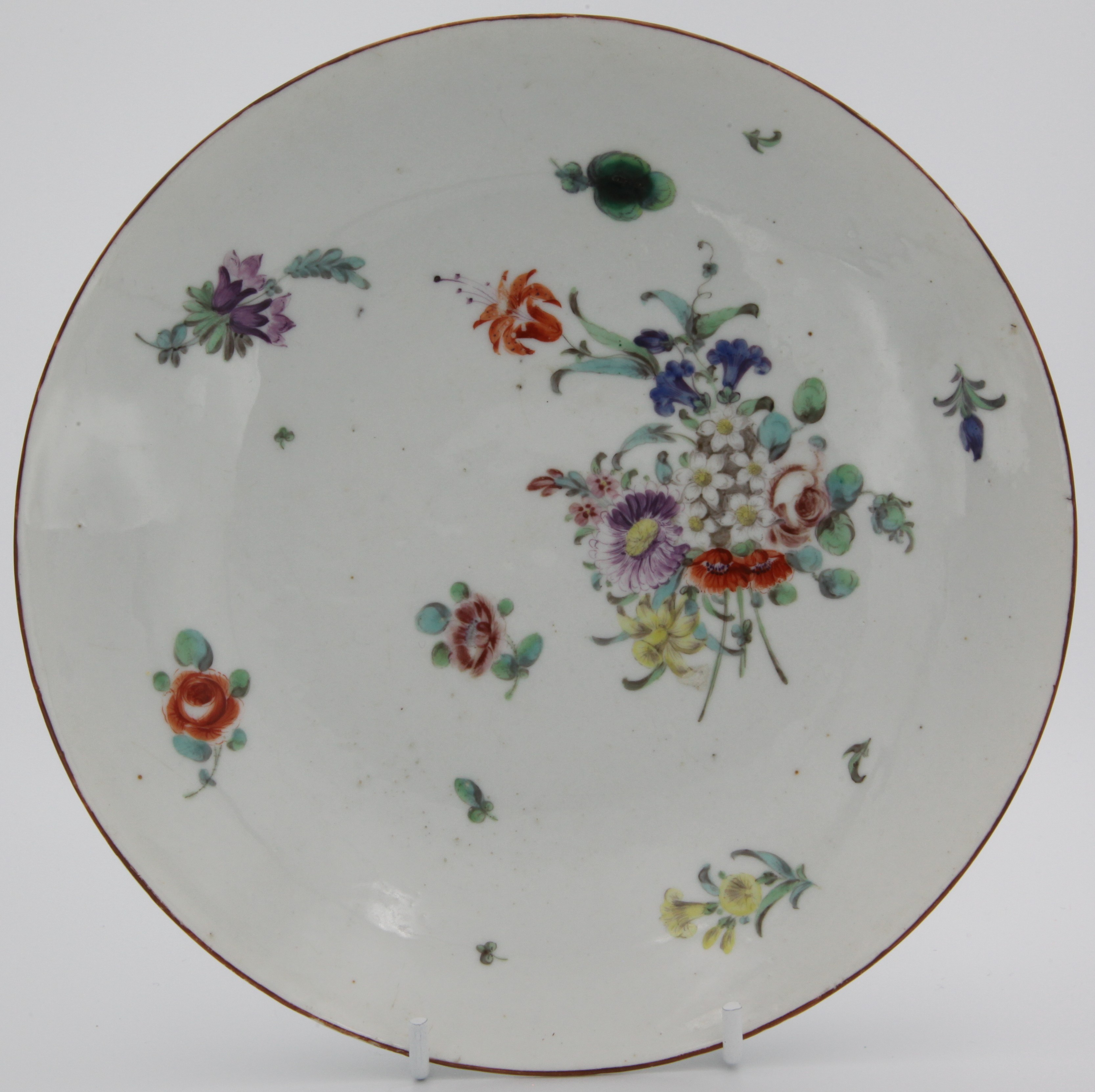 A large Bristol saucer dish painted with a bouquet of flowers and scattered sprigs and leaves, blue X3 and crossed swords marks. Double reinforcement on base