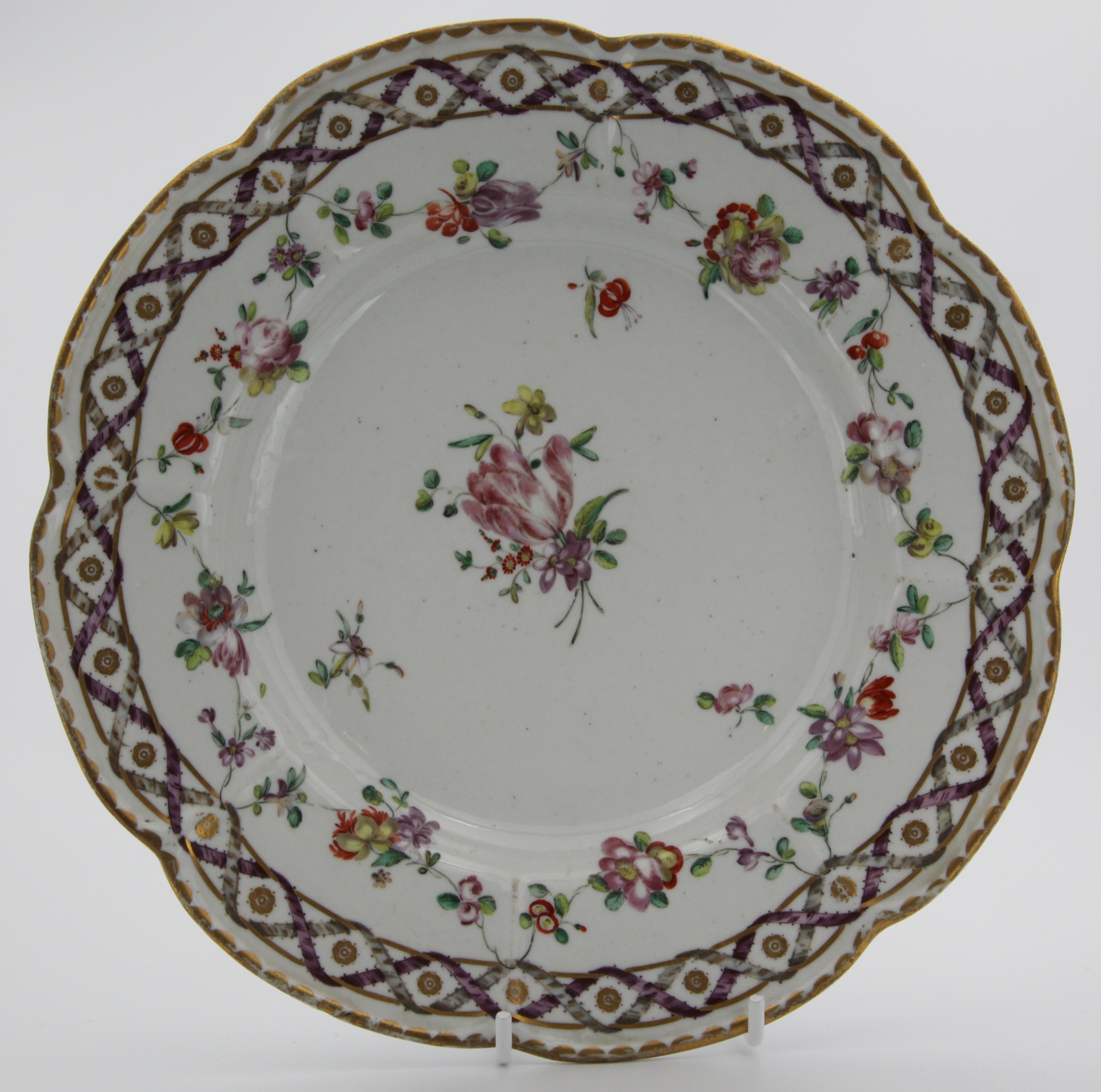 A Bristol lobed dish painted in the Sevres manner with the 'double ribbon' pattern of entwined ribbons supporting garlands of flowers around a central spray and sprigs, blue X mark with b., circa 1775-80, 23cm [minor wear].