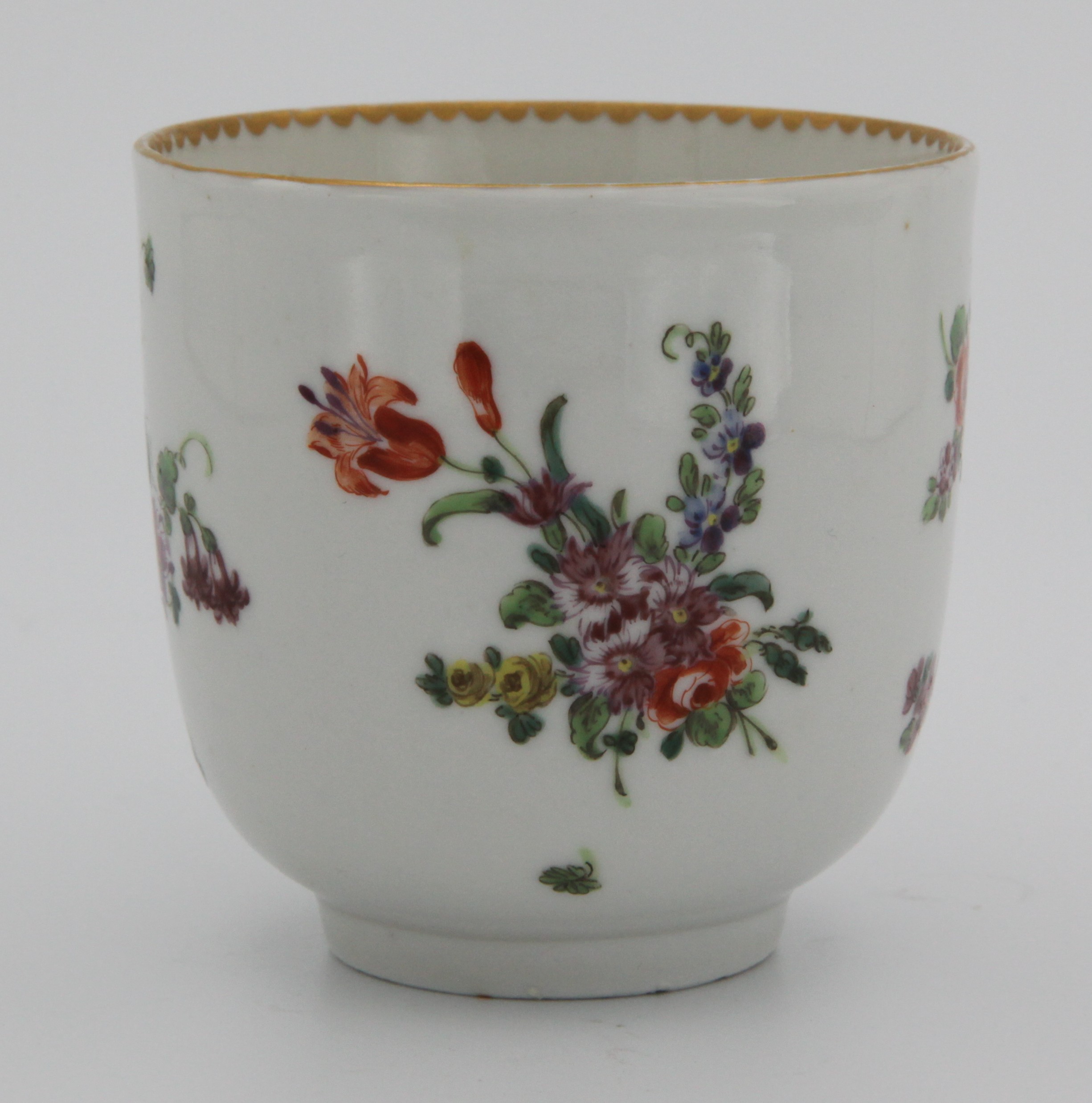 A Bristol coffee cup with rounded twig handle, painted with scattered flower sprays and sprigs with solid and dentil gilt borders, circa 1775-80. No mark. Wonky handle.