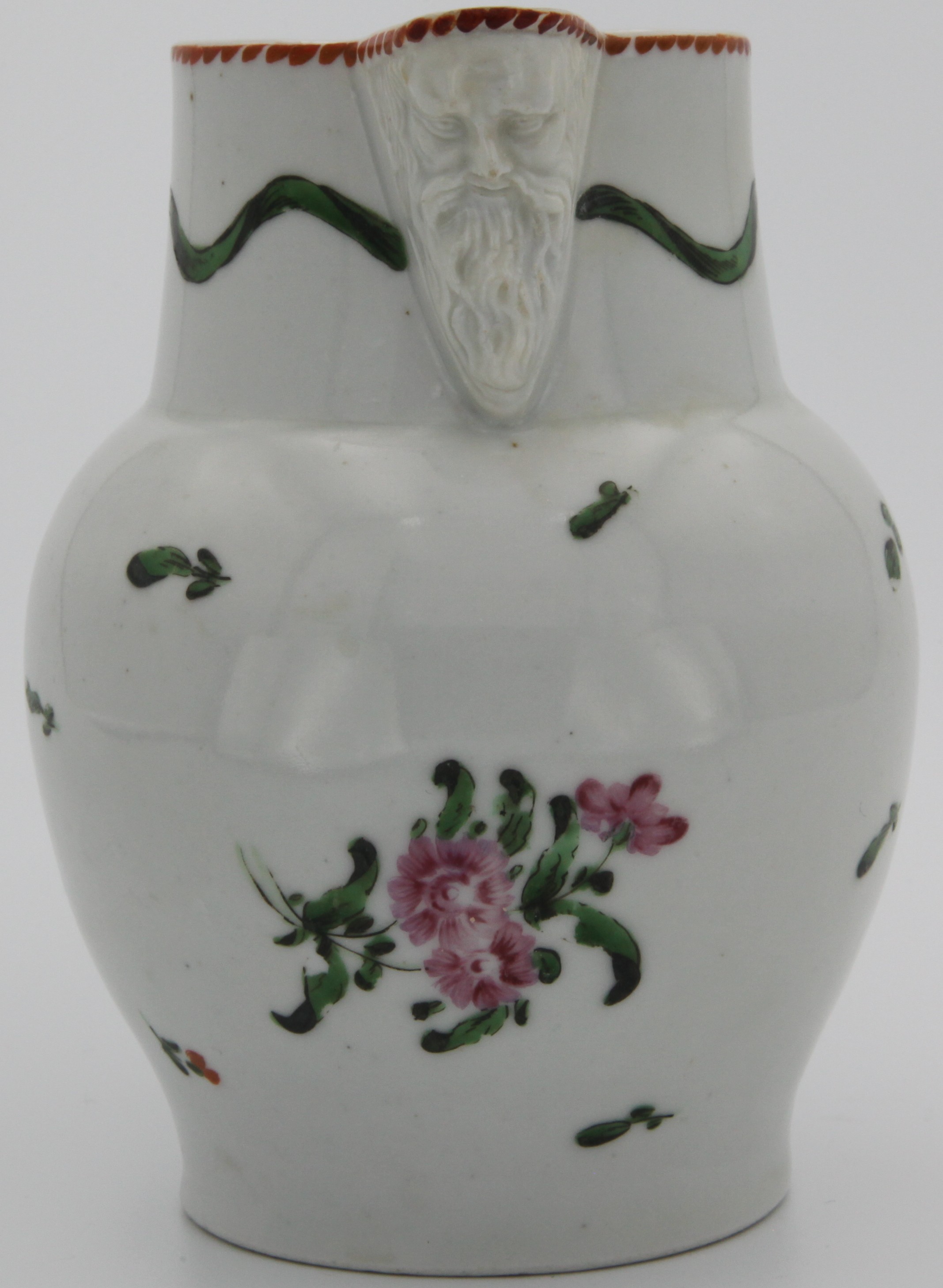 A Bristol mask jug painted with flower sprays and sprigs below a wavy band of green drapery, orange notched rim line. circa 1775. No mark