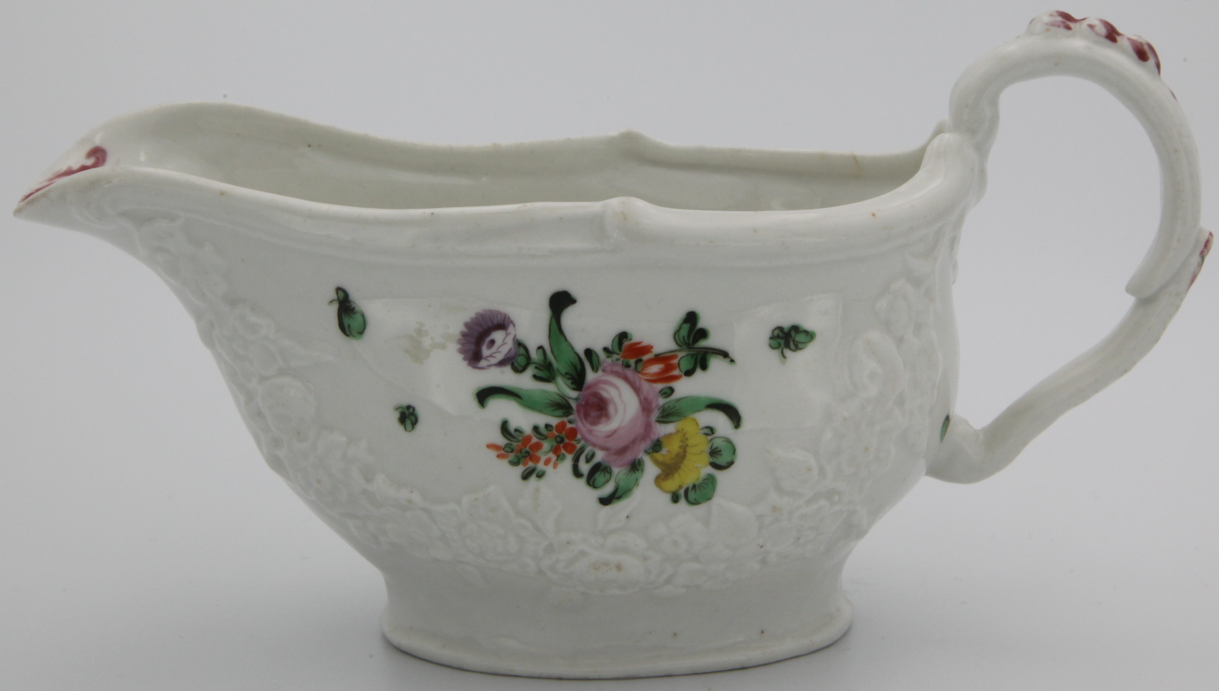 A Bristol sauceboat moulded with swags of flowers and foliage, and with moulded ear-shaped handle, the rim with scrollwork, painted with flower sprays and scattered green leaves, circa 1775. No mark