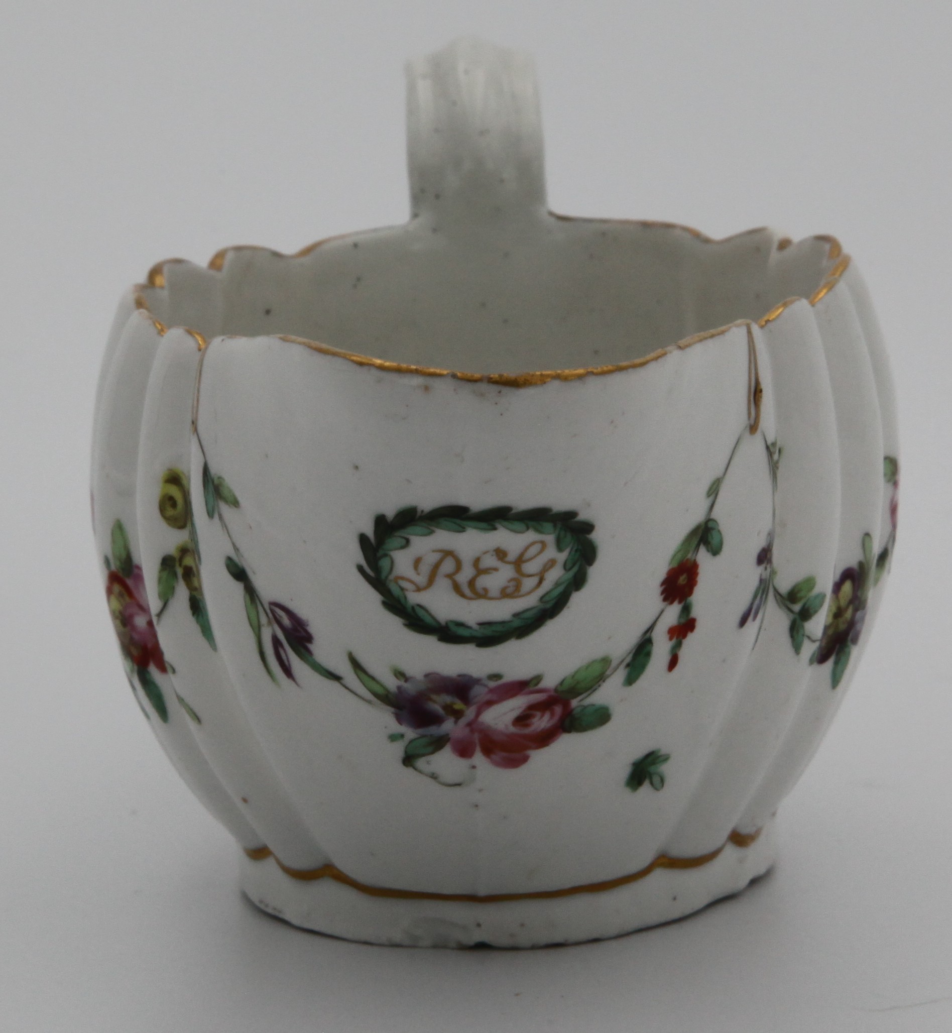 A Bristol fluted oval sauceboat monogrammed 'REG' in gilt within a leafy roundel, painted with garlands of flowers suspended from gilt loops hanging from gilt rim line, X10 mark, circa 1775-80.