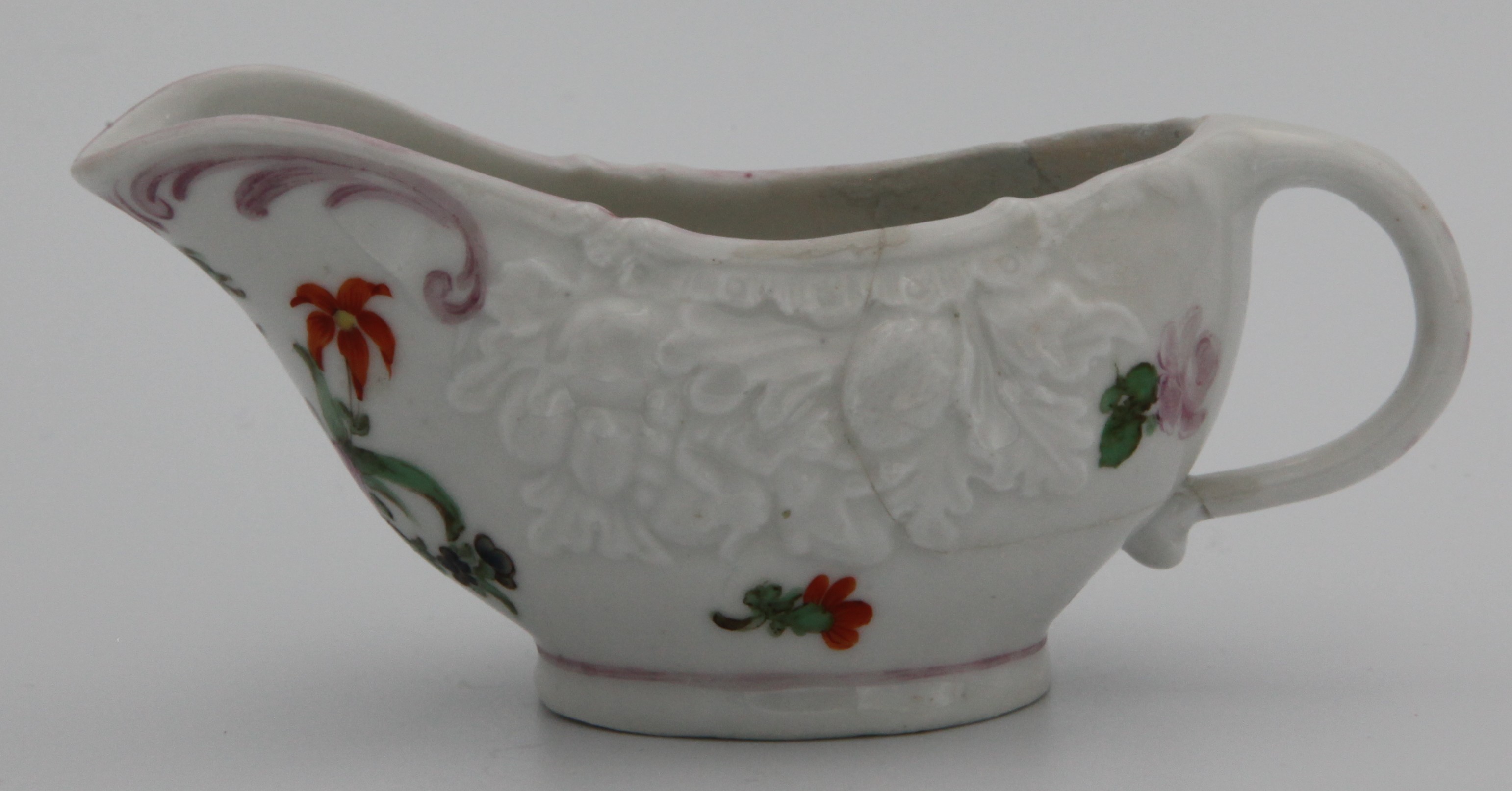 A Bristol butterboat moulded with bunches of fruit and painted with a loose bouquet and sprigs, plain handle painted in puce, puce scroll decoration under lip and puce line above base, circa 1775-80. No mark