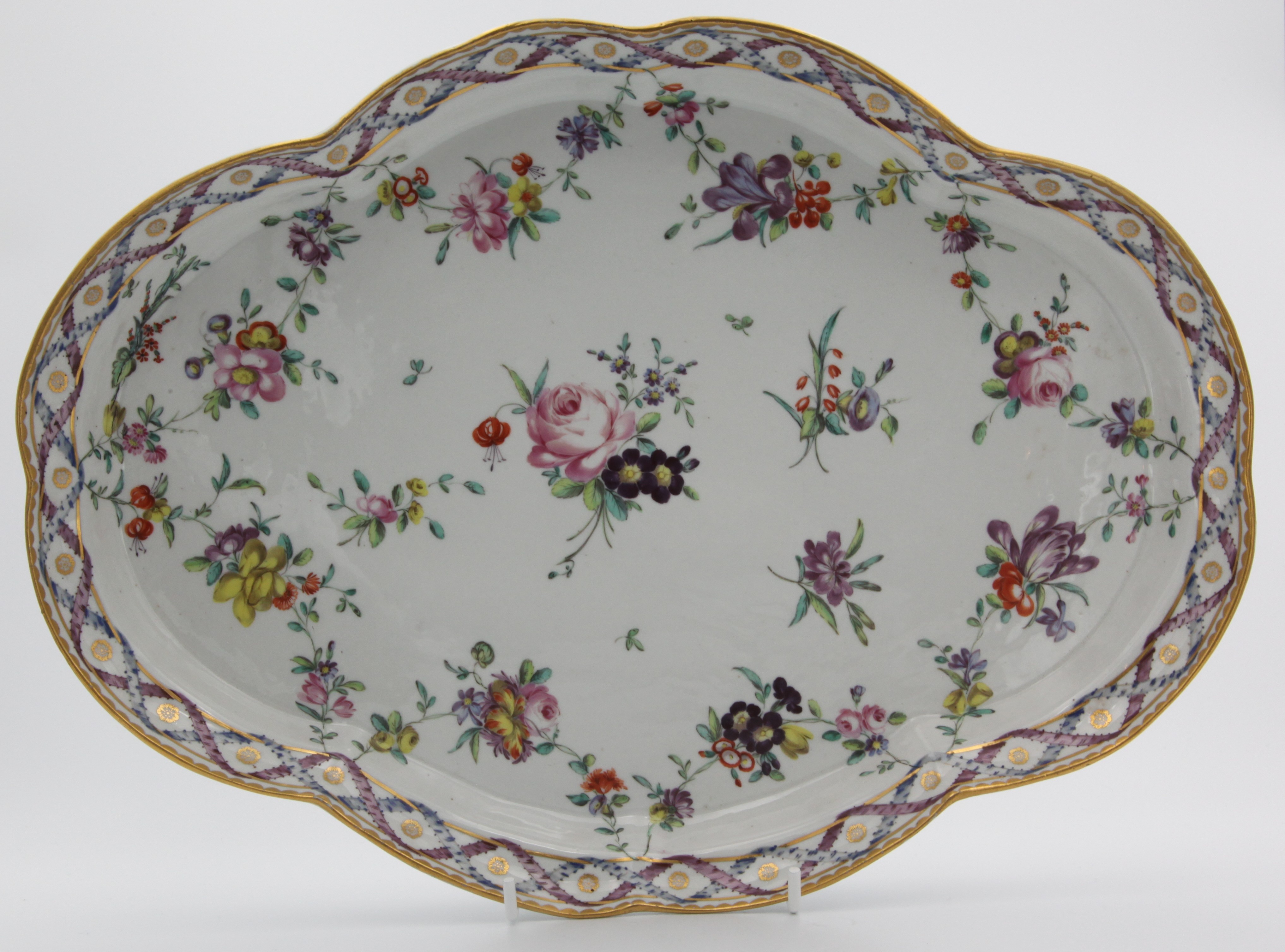 A Champion's Bristol shaped oval tray painted in the 'double ribbon' pattern of flower sprays and garlands suspended from entwined blue and puce ribbons, gilt dentil rim, blue X mark with faint 1 in gilt, circa 1775-80.