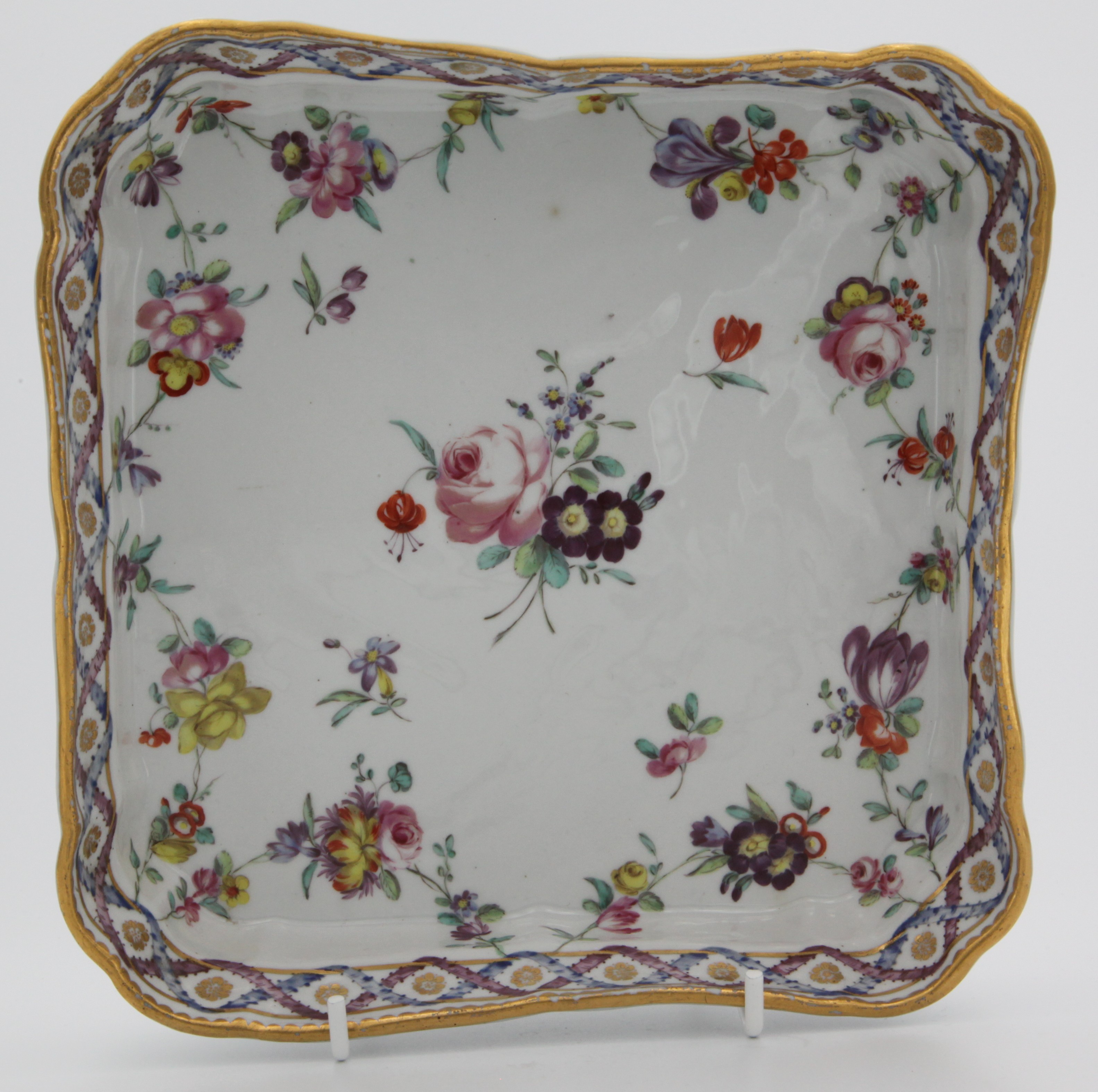A rare Bristol square dessert dish, painted in coloured enamels with a flower spray and scattered flowers, the puce and blue interlocked border with gilt flower head medallions, and suspending swags of flowers and leaves, gilt dentil rim, circa 1775, blue painted X mark and letter b in gilt. See Albert Amor, The Alfred Trapnell Collection, 1912, numbers 170-181 for a part dessert service in this pattern, but not including the square dishes. A pair of Bristol shell-shaped dishes in this pattern was exhibited Albert Amor, the Vanessa Stevenson Collection, 2021, number 45