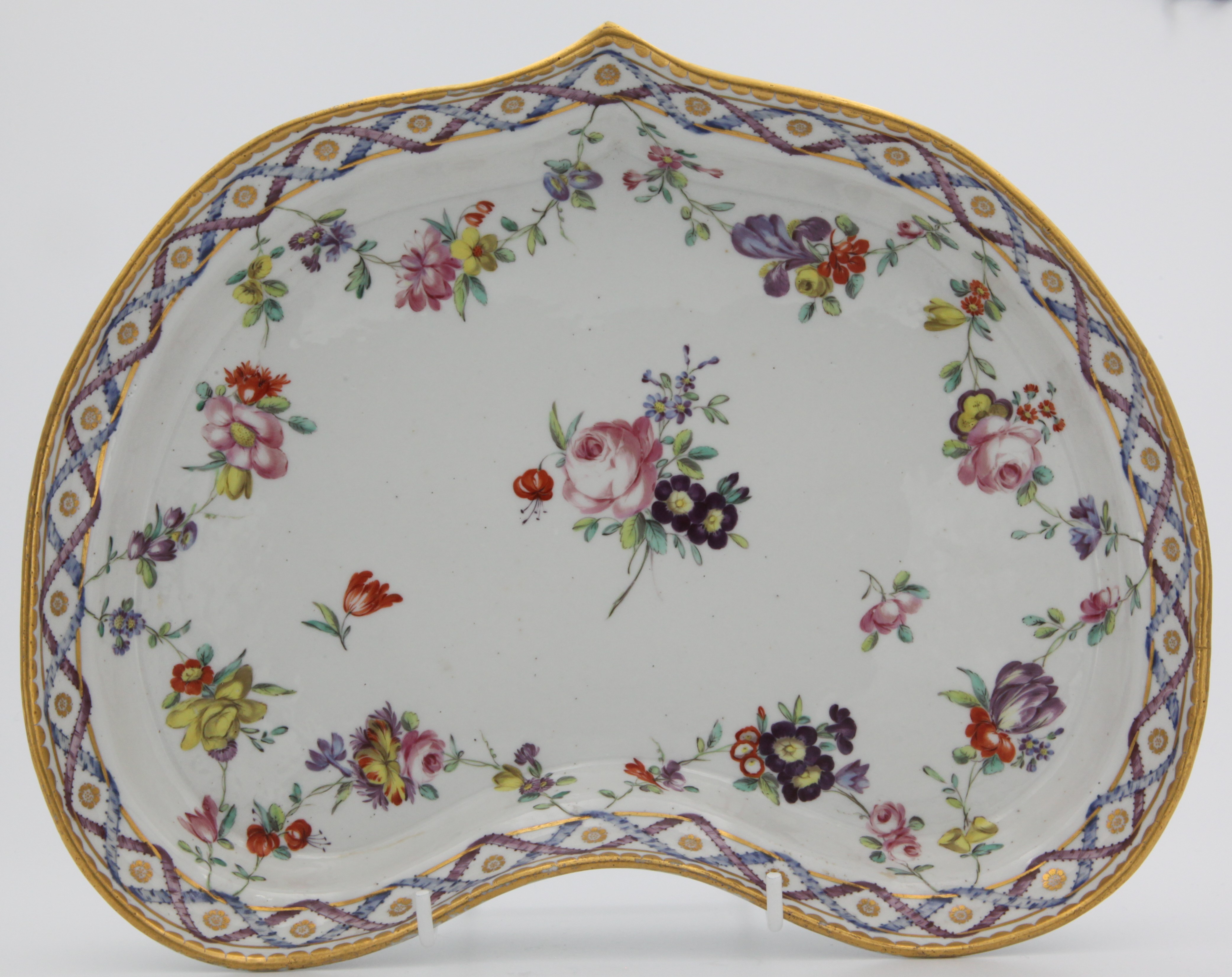 A Champion's Bristol heart-shaped dessert dish painted in the 'double ribbon' pattern of flower sprays and garlands of flowers suspended from entwined blue and puce ribbons, gilt dentil rim, blue Xb. mark with 6 in gilt, circa 1775-80. Very interesting reinforcement on base