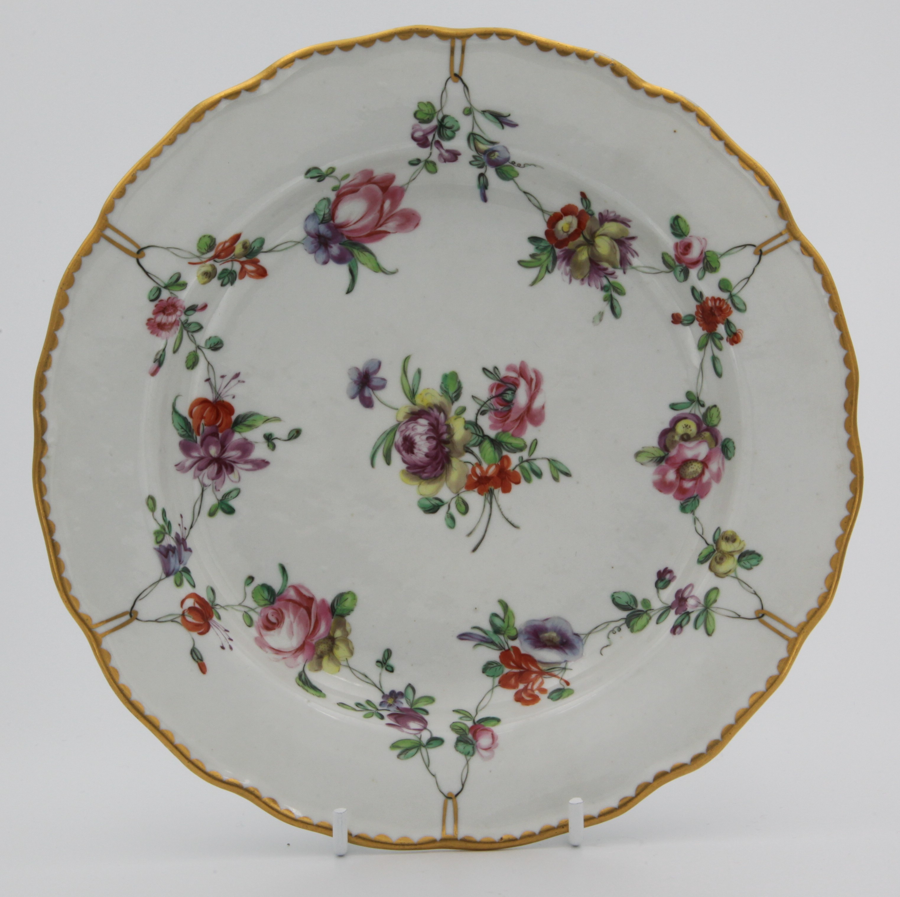 A fine Bristol plate painted with garlands of flowers suspended from gilt rings around a central bouquet, gilt dentil rim, blue Xb mark, circa 1775-80. Double reinforcement ring to base. Same as 1243 and 1244