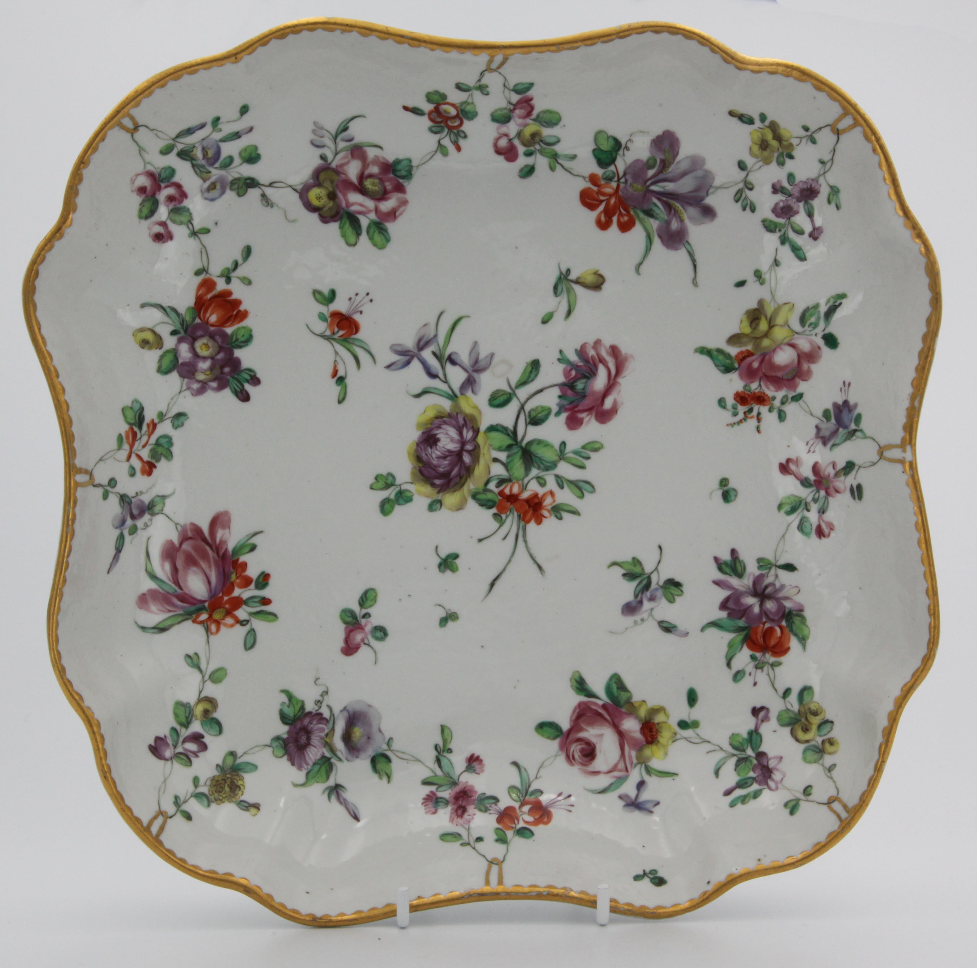 A large Bristol square lobed dish, the shaped rims with gilt dentil edging supporting polychrome flower swags with central spray. Blue X grey b