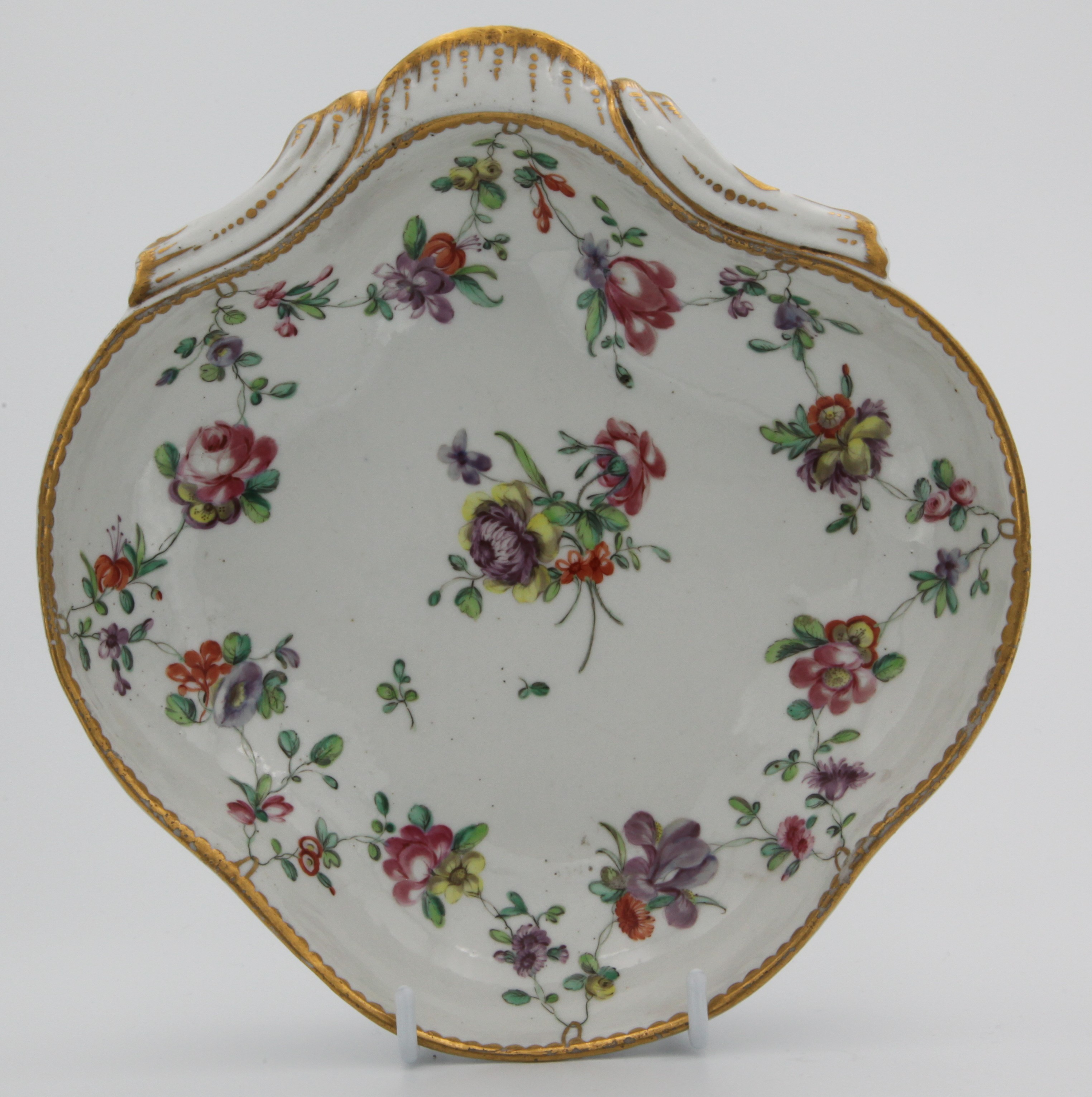 A fine Bristol shell-shaped dessert dish, the shaped rim with gilt dentil edging supporting polychrome flower swags with central spray. Blue Xb mark. Trapnell label lot 95 or 96