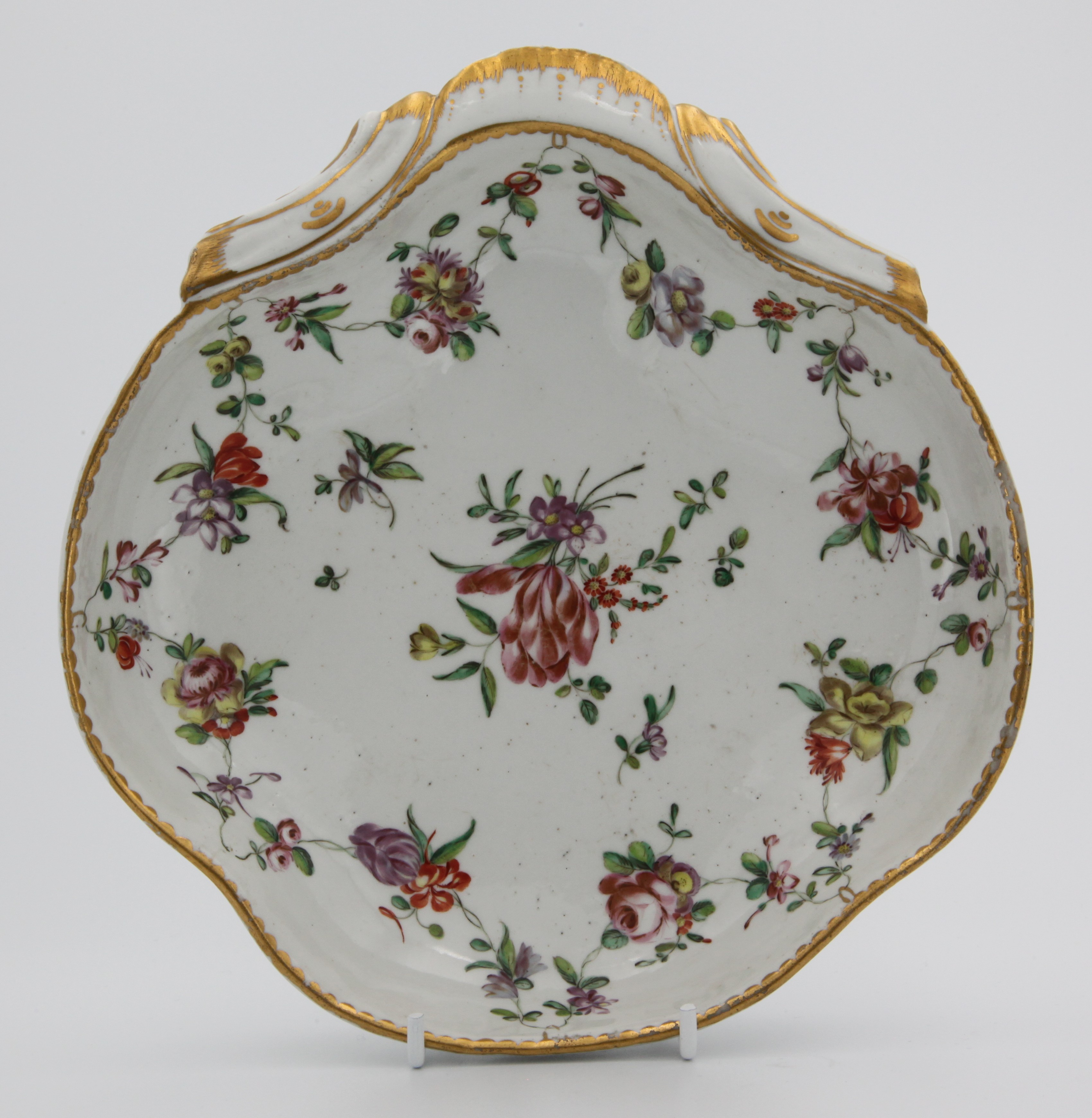 A fine Bristol shell-shaped dessert dish, the shaped rim with gilt dentil edging supporting polychrome flower swags with central spray. No mark. Trapnell label lot 95 or 96