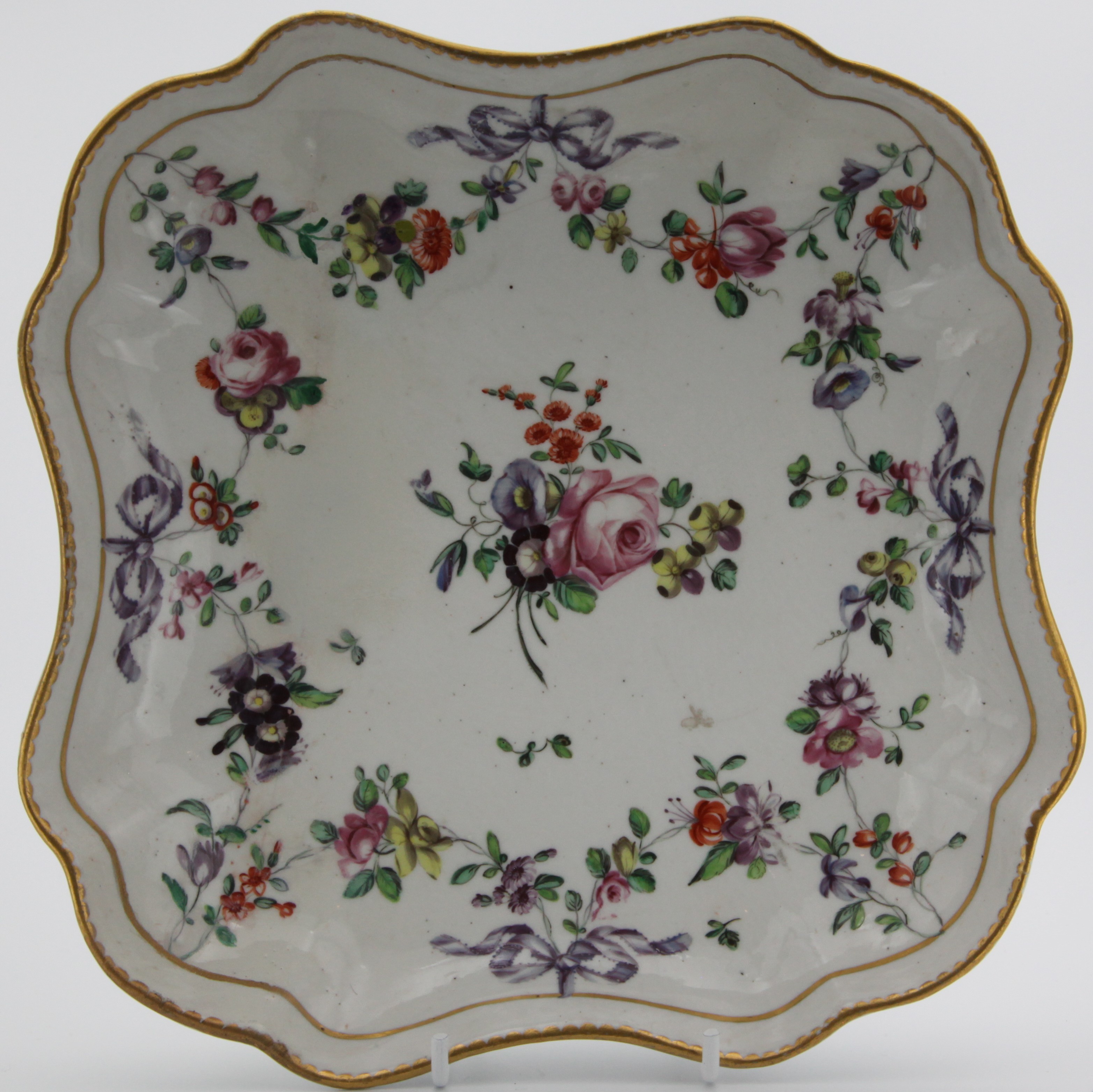 A Bristol square dish, painted in enamels with a colouful floral garland suspended from a gilt band and from purple ribbons, with central floral spray, all within gilt dentil rims. blue Xb mark