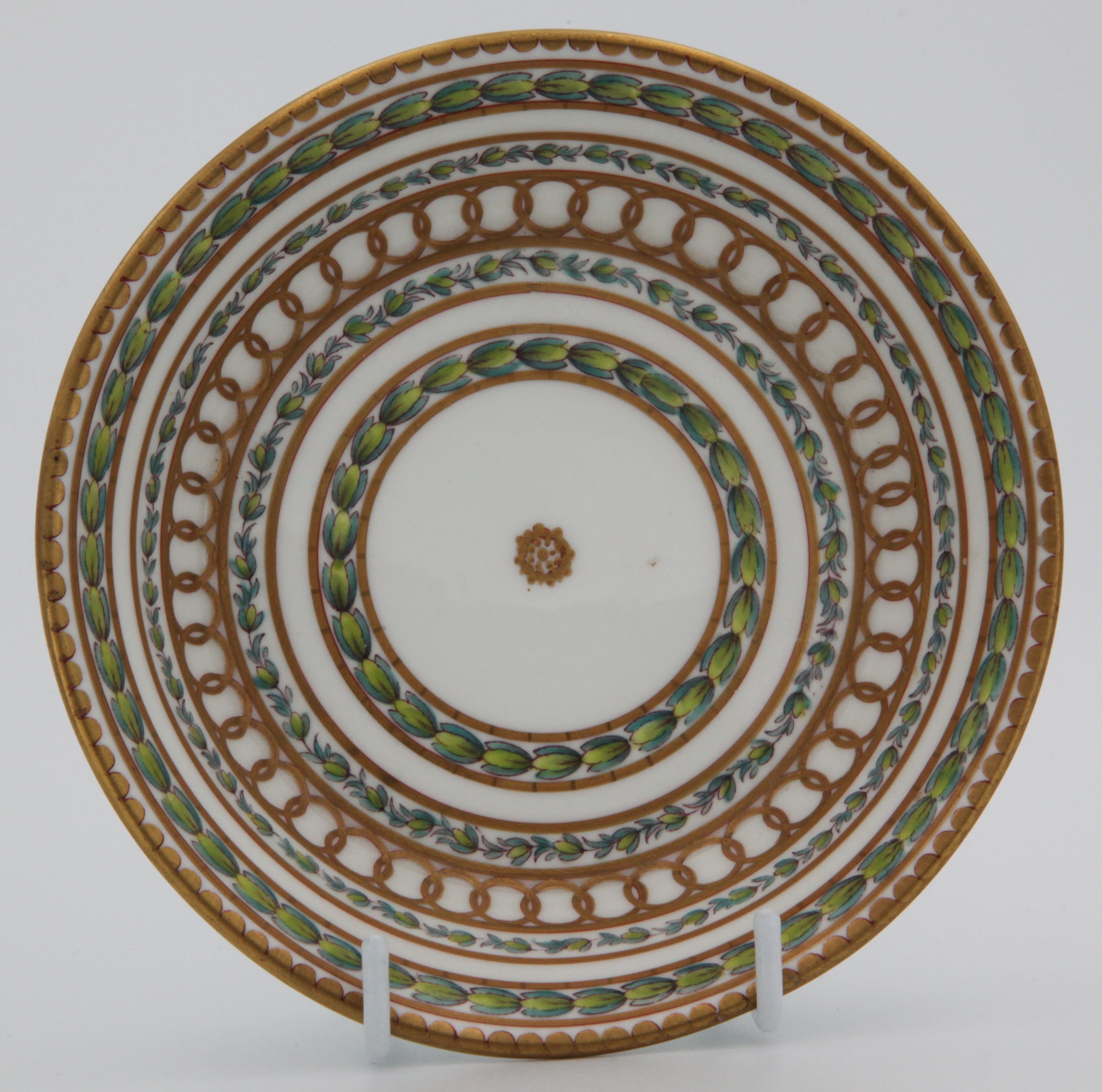 Saucer for Bristol cabinet cup with bands of gilding and laurel leaves, painted in green and puce with bands of leaves, within gilt line and interlinked roundel bands, all around a central roundel and beneath gilt dentil rims,  Bristol blue X mark and numeral 1 in gilt, c.1775.