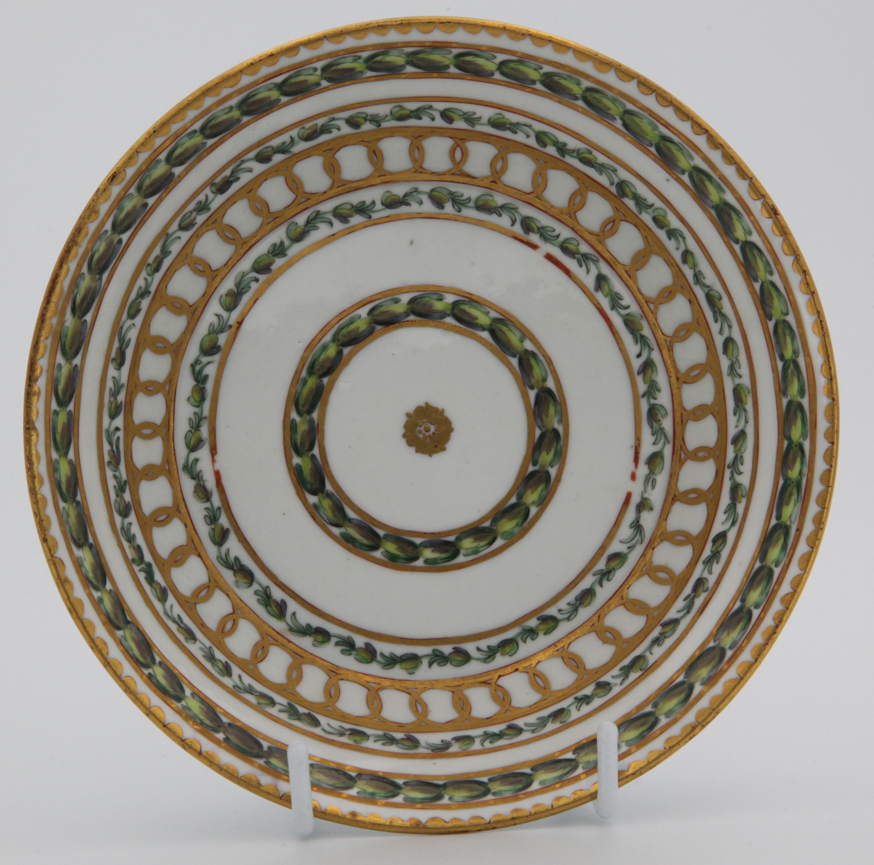 Saucer for Bristol cabinet cup with bands of gilding and laurel leaves, painted in green and puce with bands of leaves, within gilt line and interlinked roundel bands, all around a central roundel and beneath gilt dentil rims,  Bristol blue X mark and numeral 1 in gilt, c.1775.