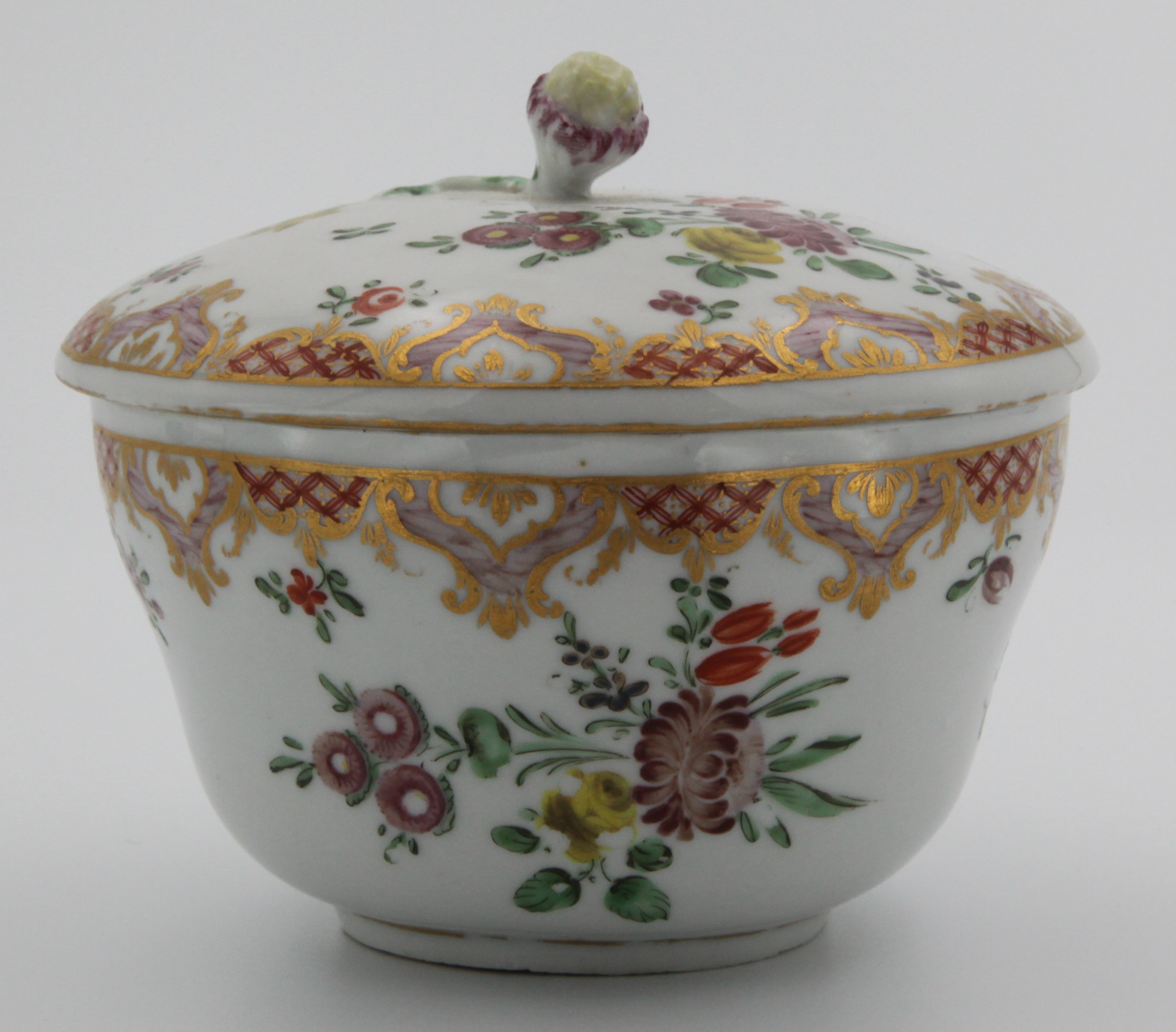 A Bristol ogee-shaped sucrier and cover, with flower and leaf knop, painted in coloured enamels in Ludlow service style, with flower sprays, within puce scale borders, with pink and gilt cartouches of leaves and pendant flowers, circa 1775, no mark.