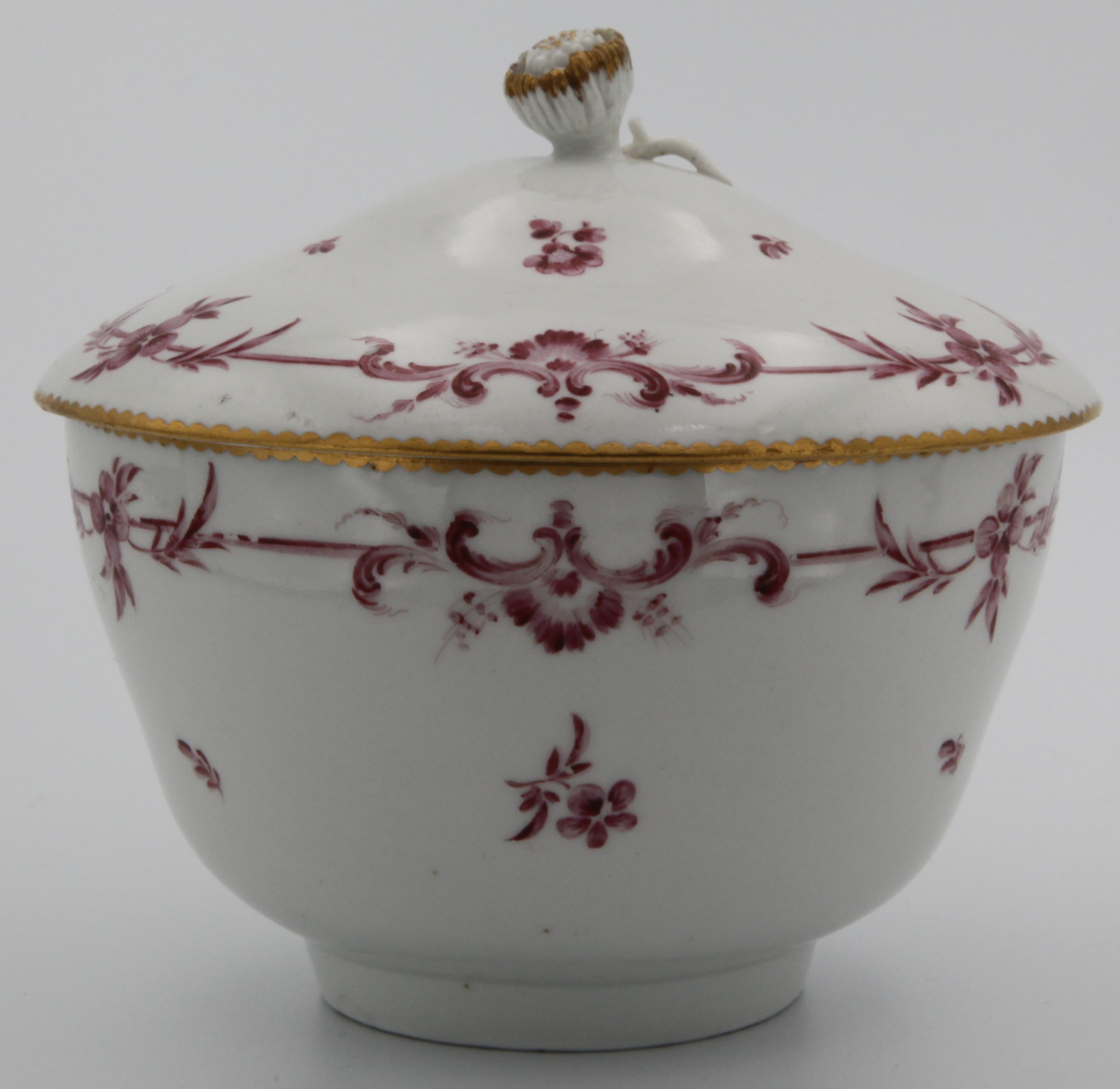 A fine Bristol porcelain ogee-shaped sucrier and cover, the cover with fine, gilt decorated flower knop, painted with monochrome puce scroll band with scattered flowers under gilt dentil rim. Mark: dark blue crossed swords and gilt 6.