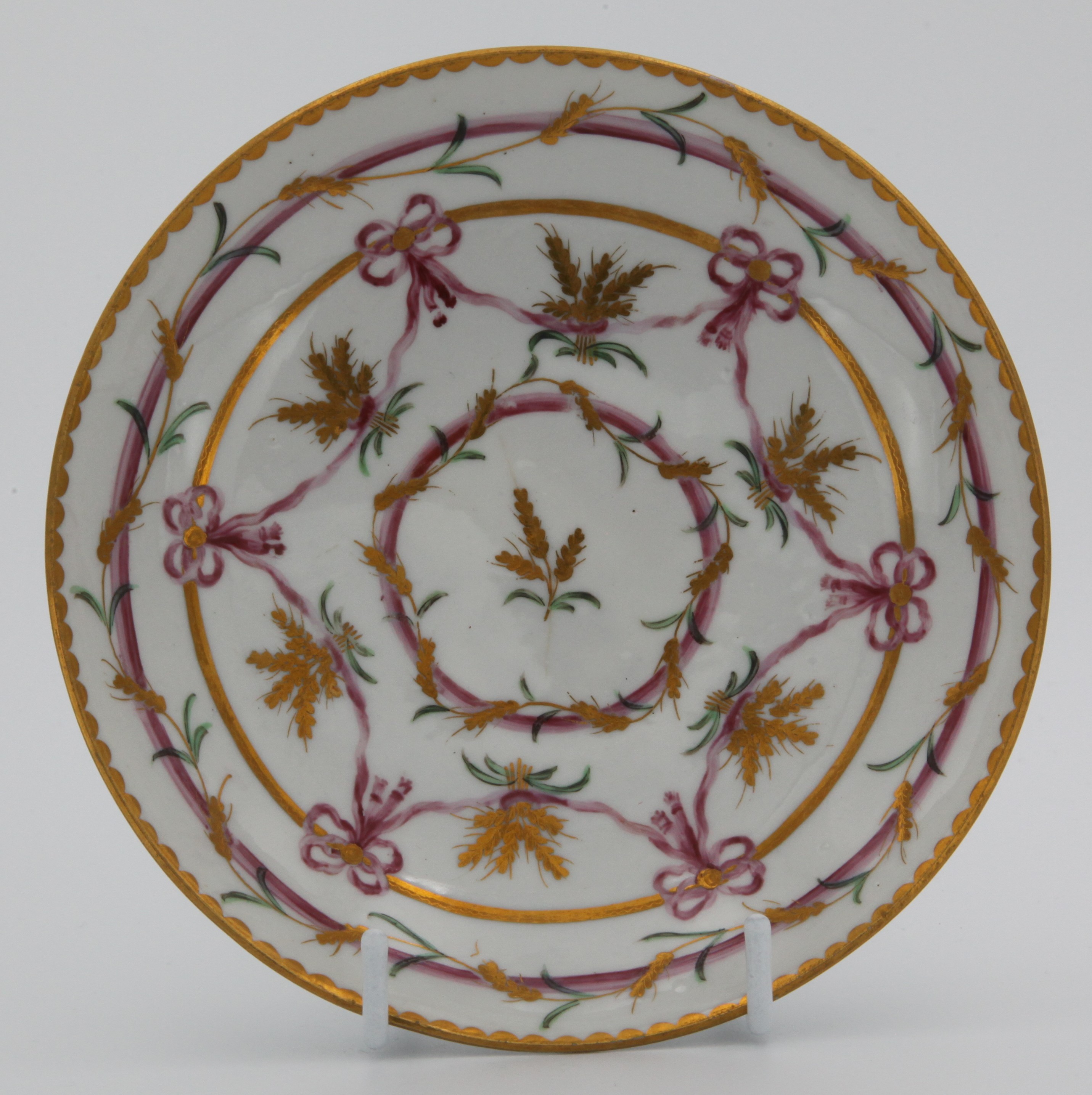 A rare Bristol ogee-shaped tea saucer from the Butts service, painted in pink and gilt with wheat ears, lopped ribbons and bands, gilt dentil rims, circa 1775.  Blue X10 on saucer. See FS Mackenna, Plymouth and Bristol Porcelain, figures 49 and 50 for the slop bowl and a teacup and saucer from this service.