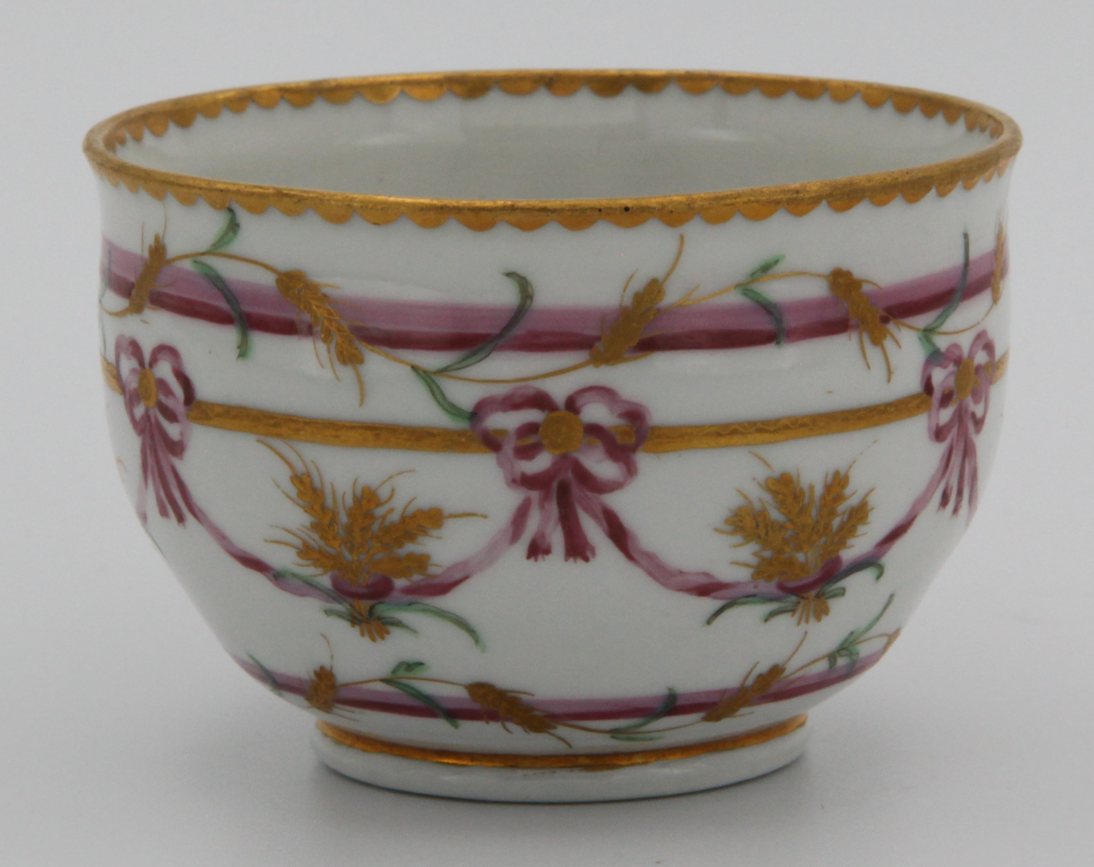A rare Bristol ogee-shaped teacup from the Butts service, with ear-shaped handle, painted in pink and gilt with wheat ears, lopped ribbons and bands, gilt dentil rims, circa 1775. Blue X gilt 10.  See FS Mackenna, Plymouth and Bristol Porcelain, figures 49 and 50 for the slop bowl and a teacup and saucer from this service.