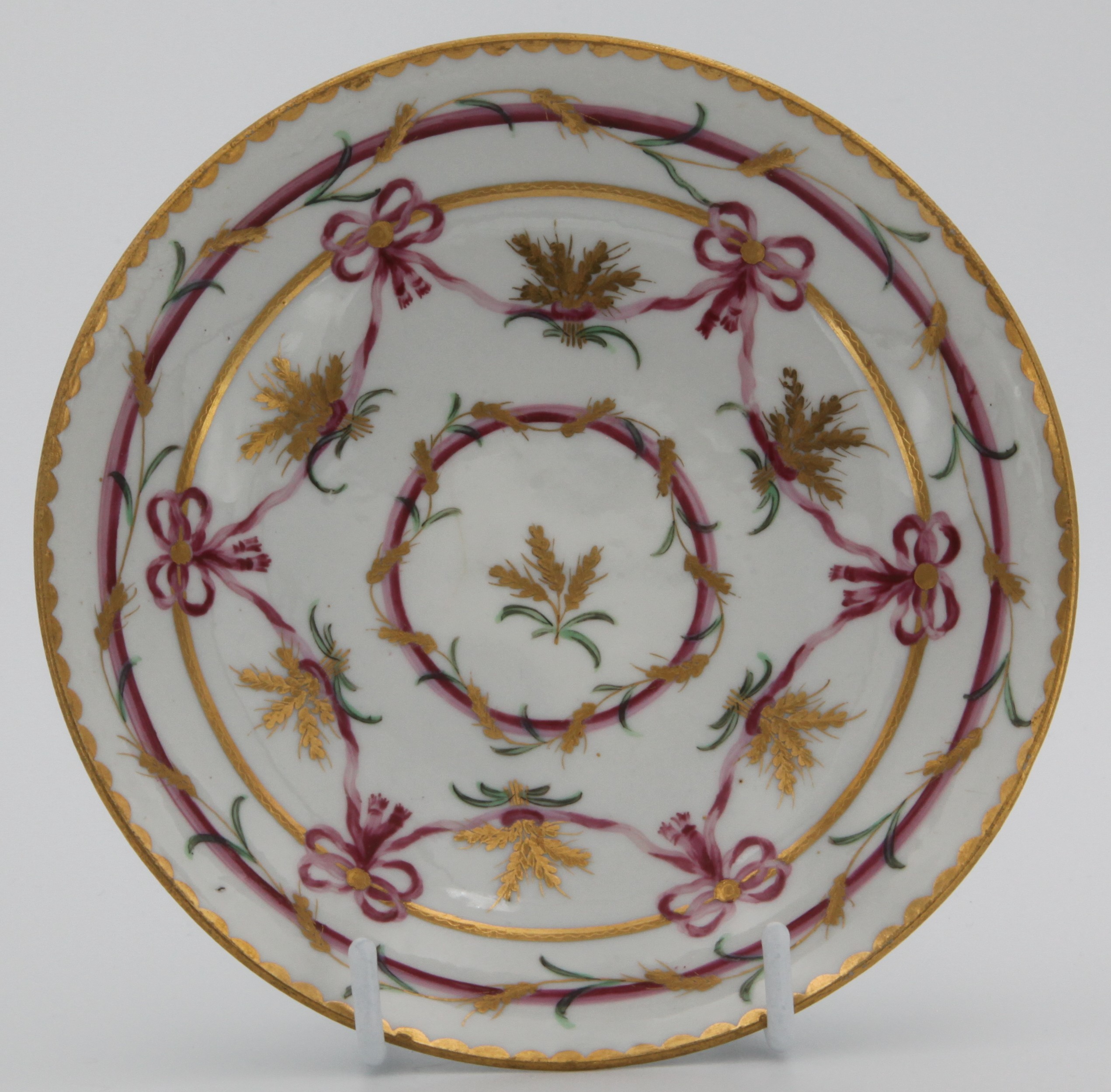 A rare Bristol ogee-shaped tea saucer from the Butts service, painted in pink and gilt with wheat ears, lopped ribbons and bands, gilt dentil rims, circa 1775.  Blue X10 on saucer. See FS Mackenna, Plymouth and Bristol Porcelain, figures 49 and 50 for the slop bowl and a teacup and saucer from this service.