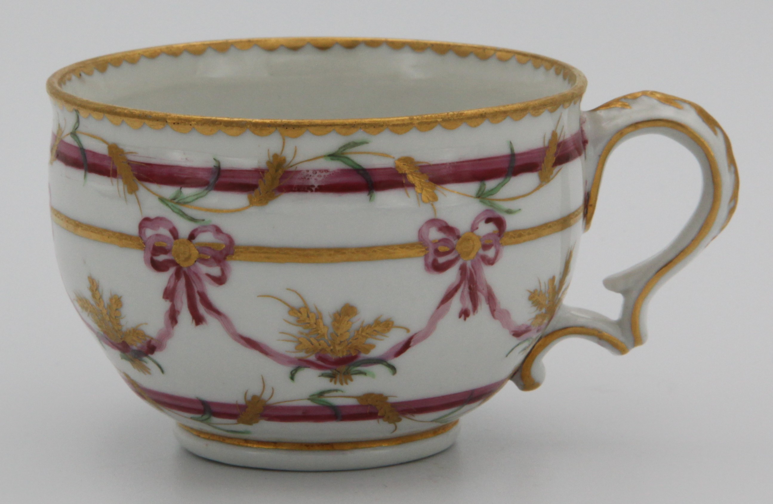 A rare Bristol ogee-shaped teacup from the Butts service, with ear-shaped handle, painted in pink and gilt with wheat ears, lopped ribbons and bands, gilt dentil rims, circa 1775. Grey X.  See FS Mackenna, Plymouth and Bristol Porcelain, figures 49 and 50 for the slop bowl and a teacup and saucer from this service.
