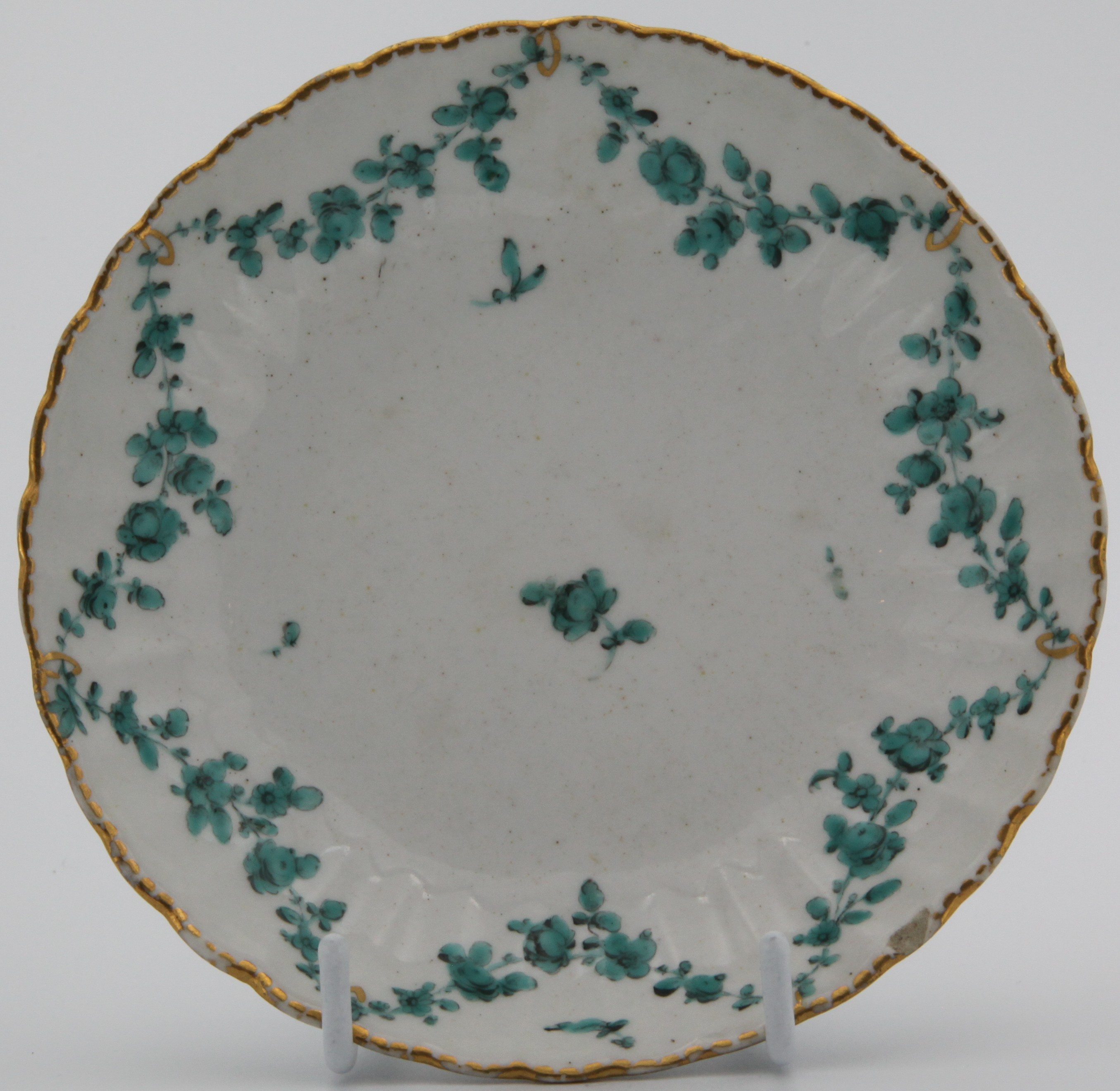 A replacement for a Bristol fluted saucer of the Horace Walpole service, with green floral swags suspended from gilt loops on gilt dentil rim, saucer 12.5cm wide cup 6cm high, no marks C.1775