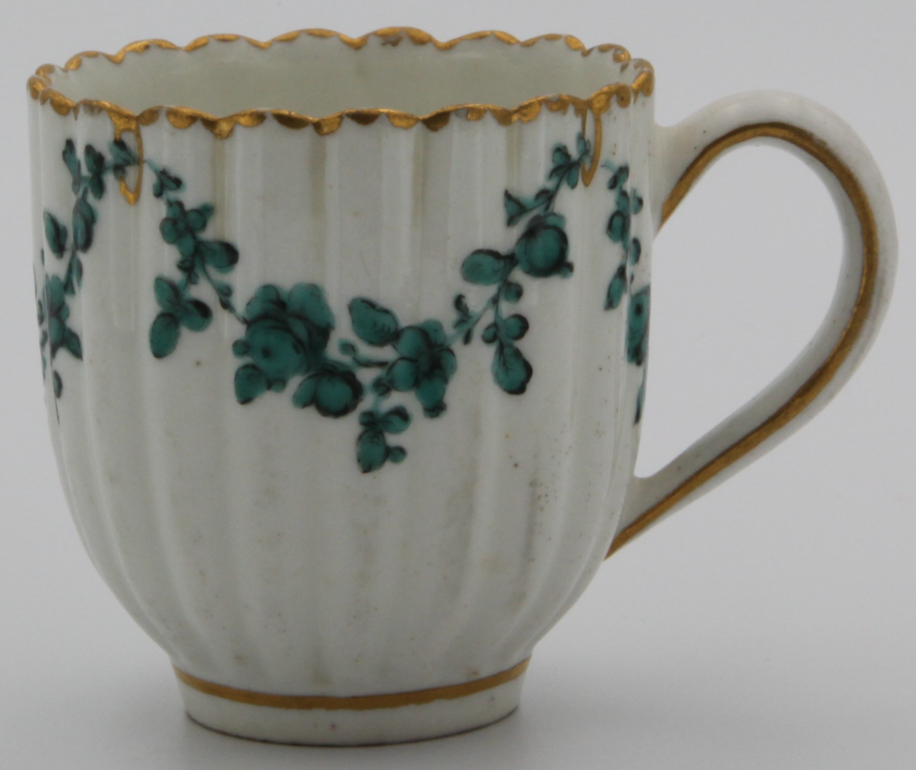 A replacement for a Bristol fluted coffee cup of the Horace Walpole service, with green floral swags suspended from gilt loops on gilt dentil rim, saucer 12.5cm wide cup 6cm high, no marks C.1775