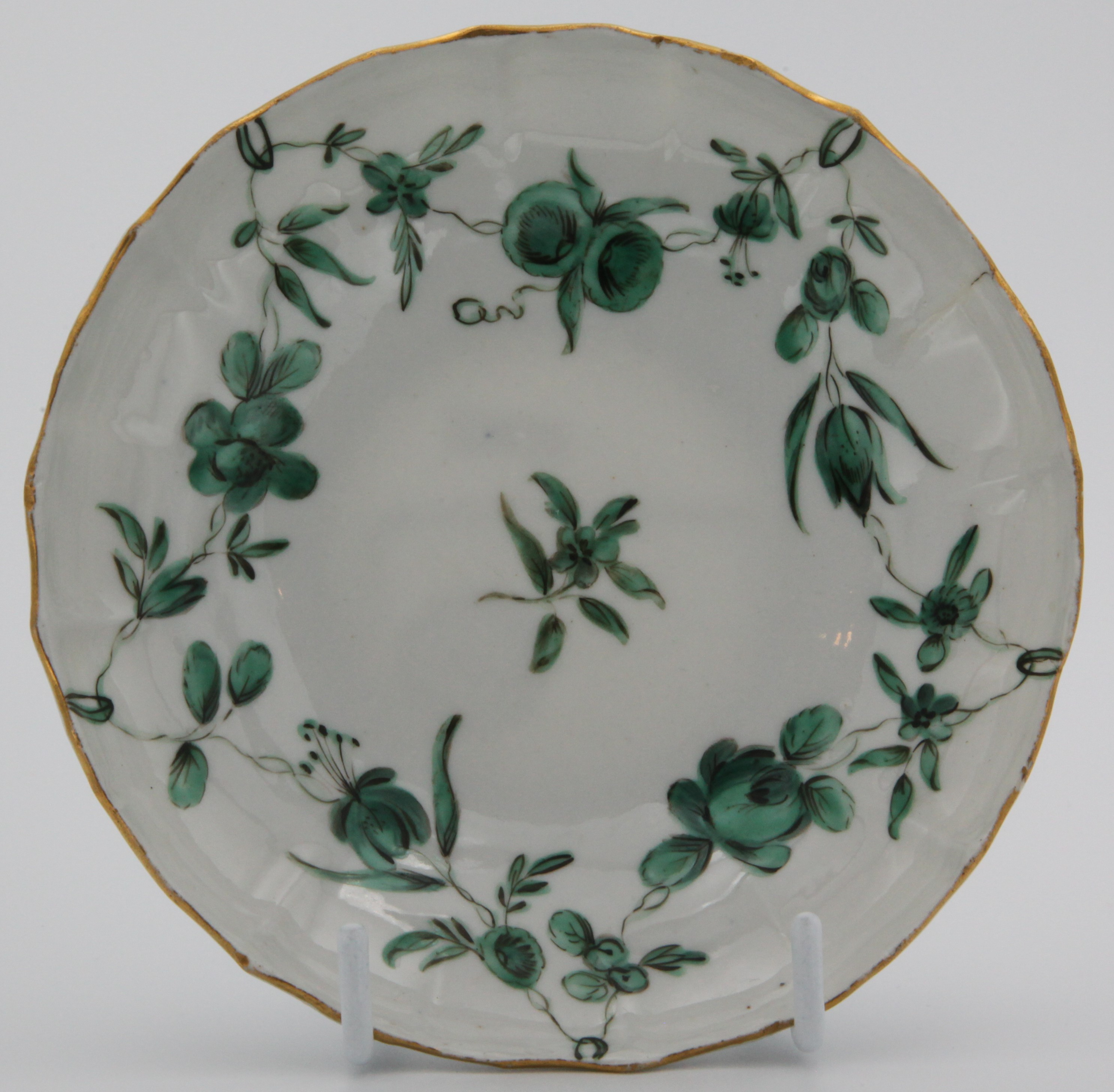 A mildly lobed Bristol coffee saucer with green vine decoration, green garlands suspended from green loops hanging from gilt rim C1780. B mark