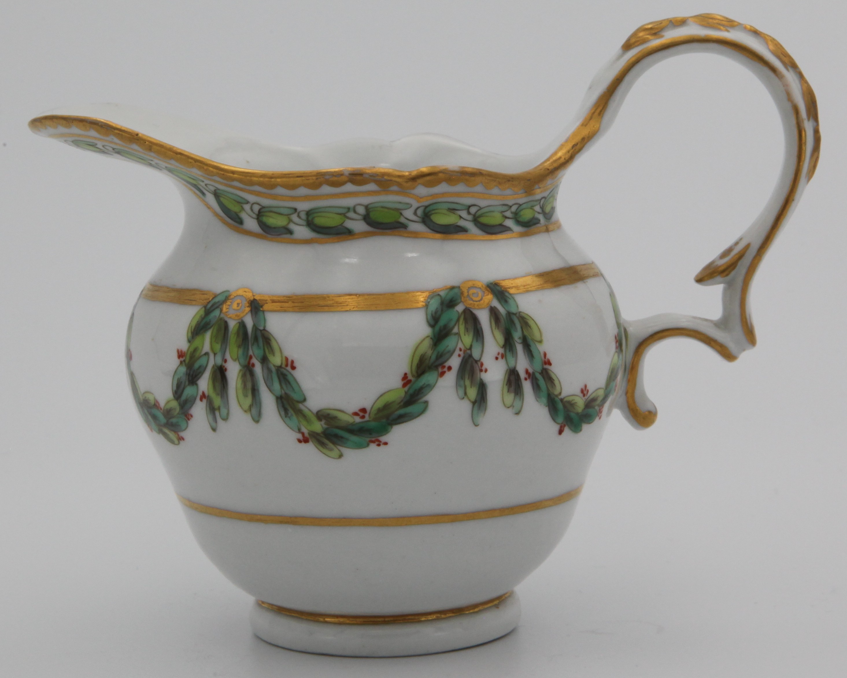 A Bristol ogee shaped milk jug, with harebell moulded scroll handle, painted in green and iron red with laurel swags, suspended from gilt roundels mounted on a heavy gilt band, within gilt line and green laurel borders, gilt dentil rim, circa 1775, blue painted X mark and numeral 1.