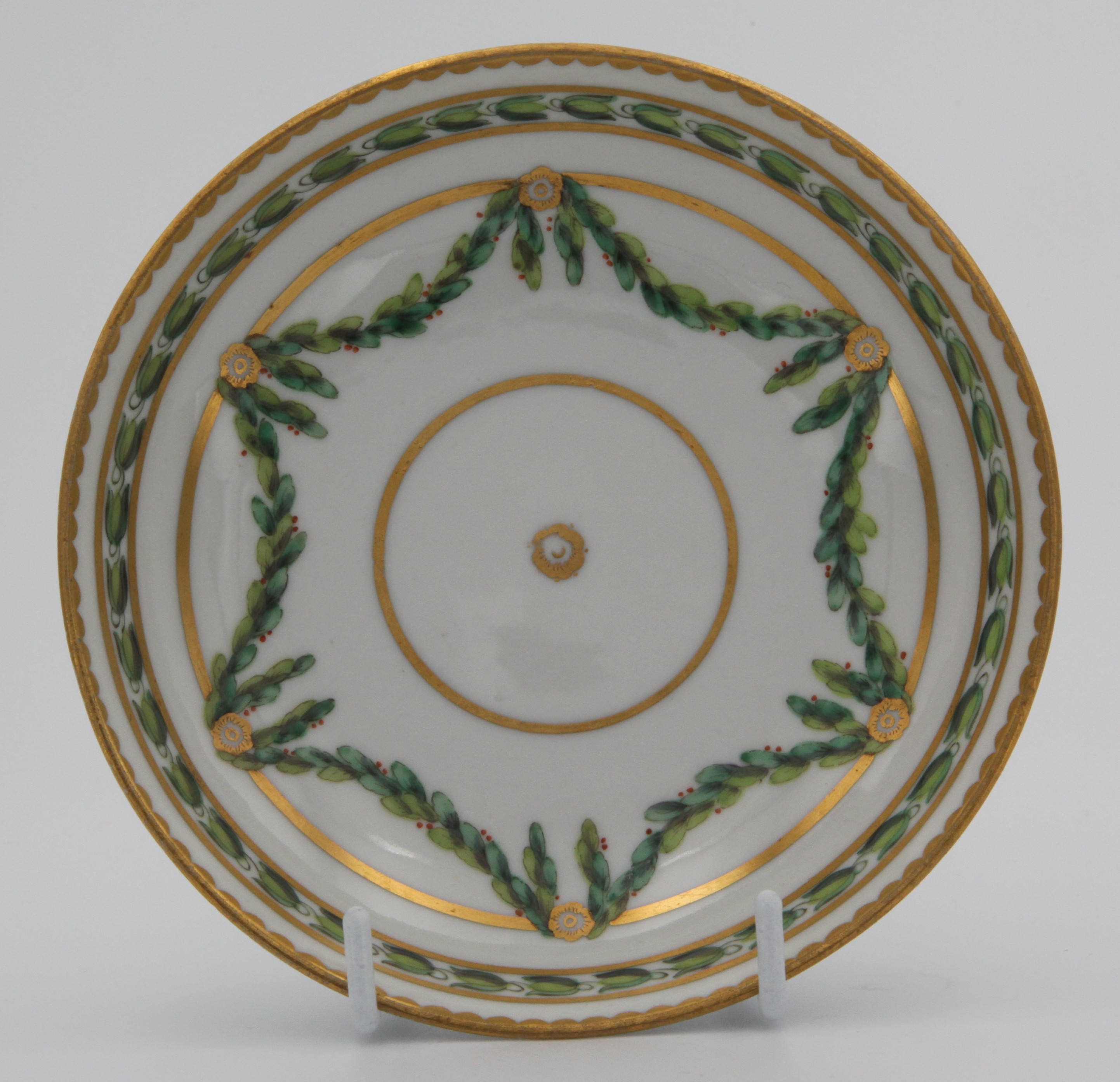 A Bristol round-shaped saucer, painted in green and iron red with laurel swags, suspended from gilt bands within green leaf scroll bands and gilt dentil rims, circa 1775, blue painted X mark.
