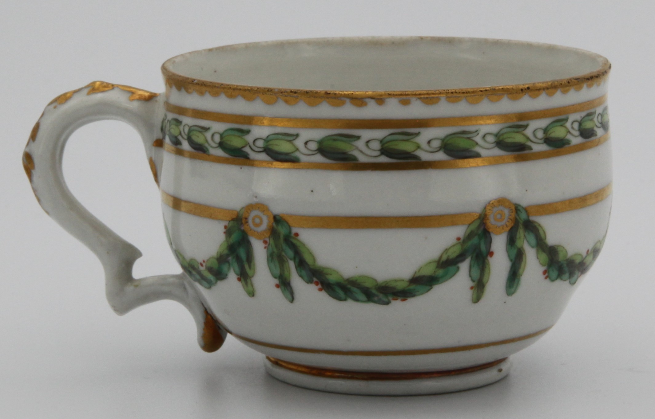 A Bristol barrel-shaped teacup with harebell-moulded ear-shaped handle, painted in green and iron red with laurel swags, suspended from gilt bands within green leaf scroll bands and gilt dentil rims, circa 1775, blue painted X mark.