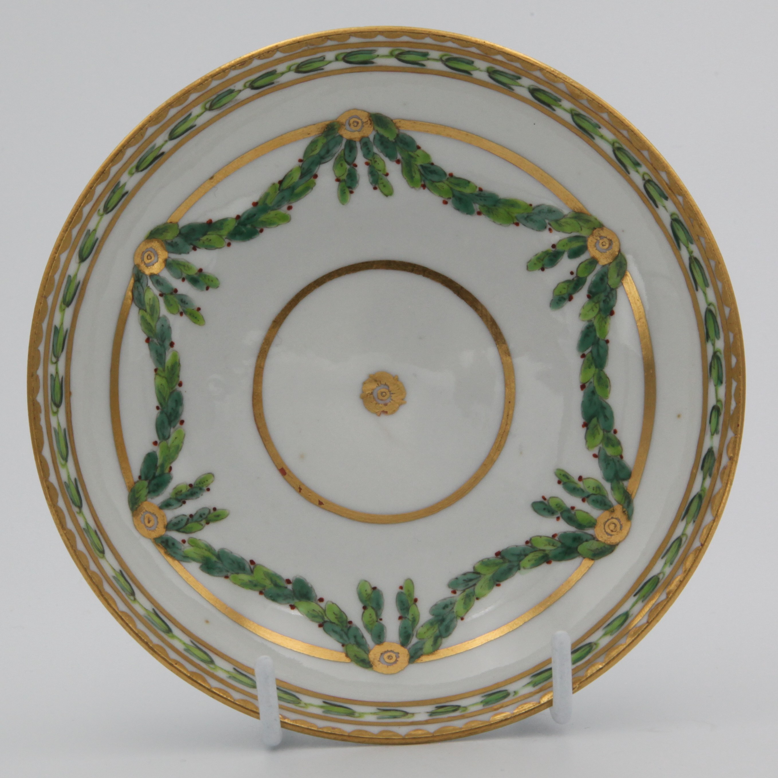 A Bristol ogee-shaped saucer, painted in green and iron red with laurel swags, suspended from gilt bands within green leaf scroll bands and gilt dentil rims, circa 1775, blue painted X mark.