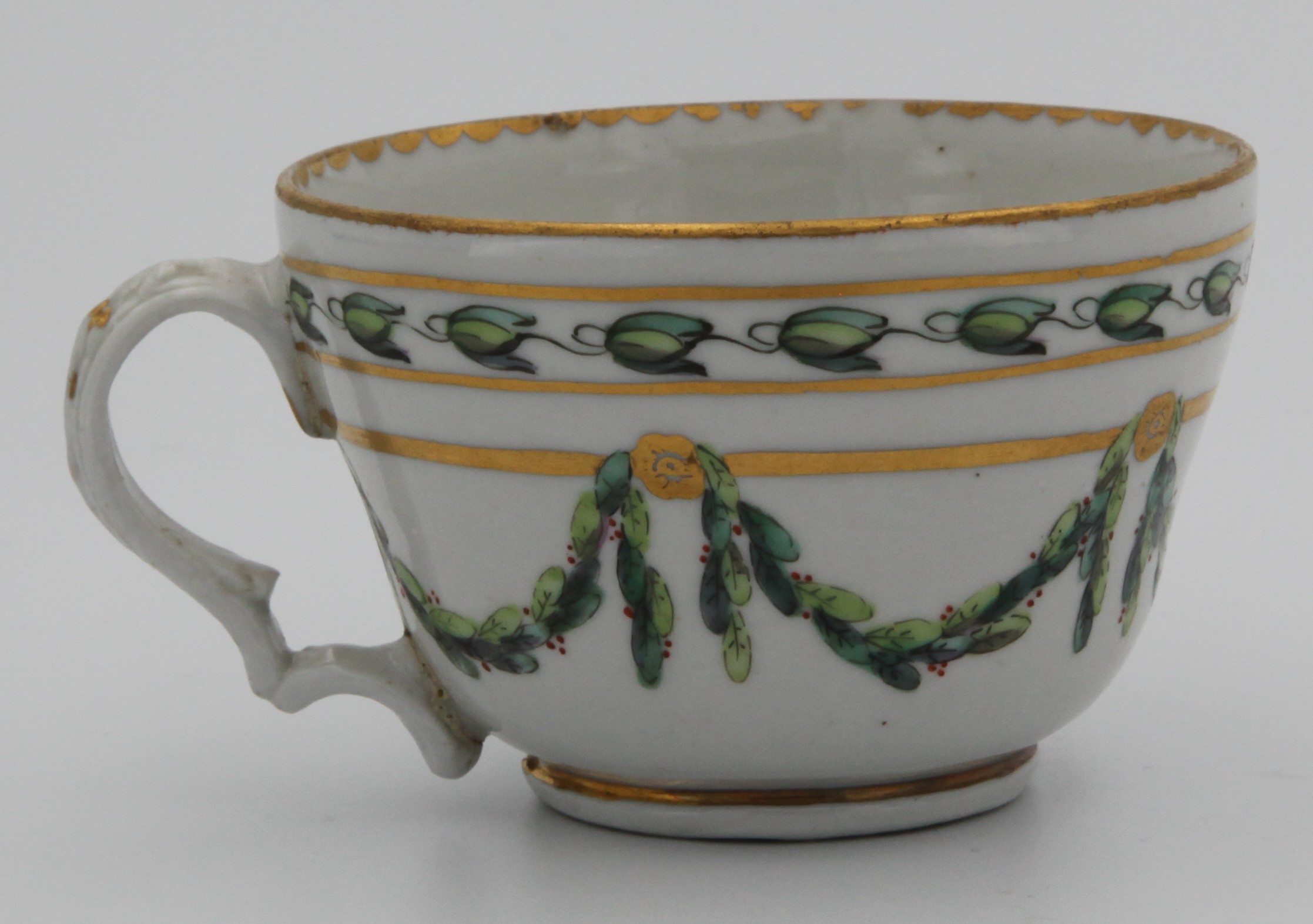 A Bristol ogee-shaped teacup with harebell-moulded ear-shaped handle, painted in green and iron red with laurel swags, suspended from gilt bands within green leaf scroll bands and gilt dentil rims, circa 1775, blue painted B mark.