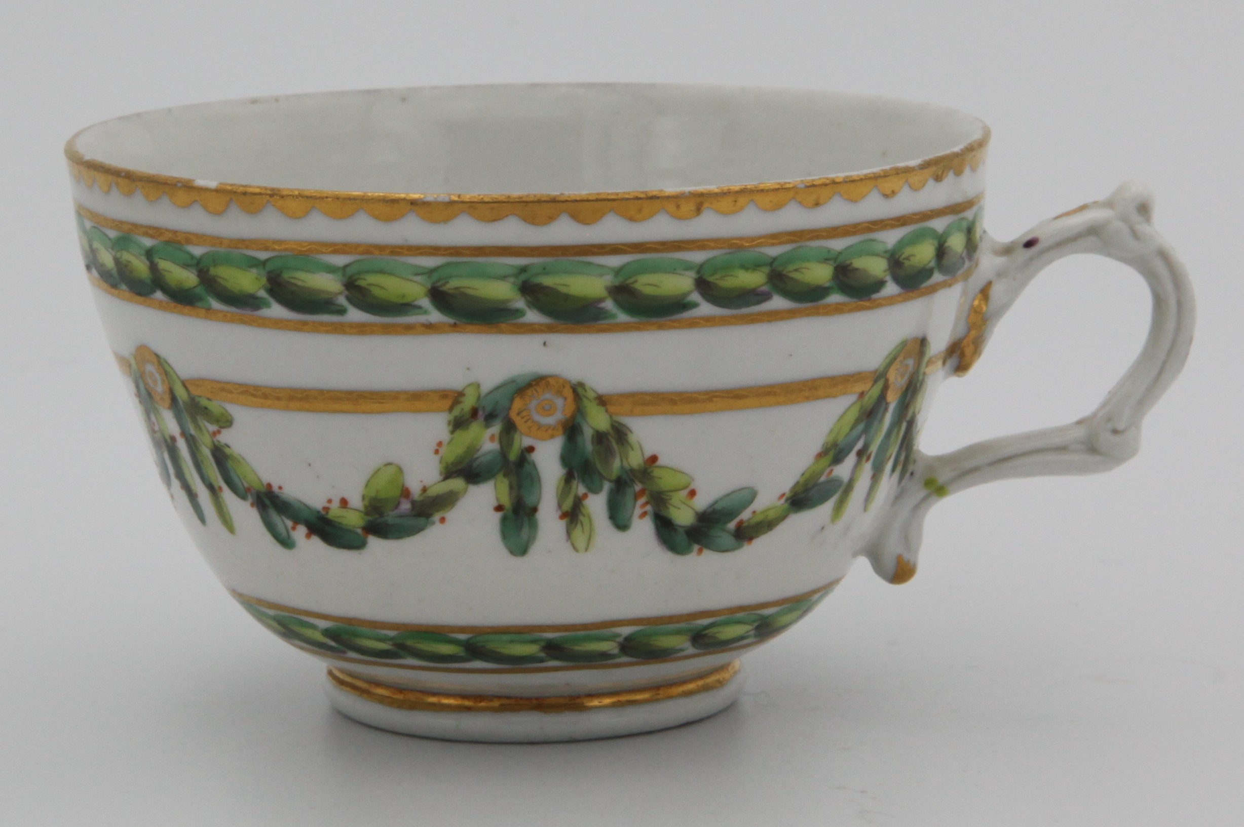 A Bristol tea cup with moulded handle, painted in green iron red and gilt with laurel garlands, suspended from roundels on gilt bands, within gilt line and dentil borders, circa 1772-75, blue painted X mark.